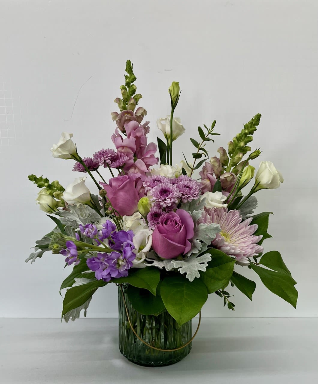 Purple Passion  - A stunning garden-style floral arrangement designed in soft shades of lavender and rich purple, beautifully accented with touches of crisp white. This romantic design features a lush mix of snapdragons, roses, stock, mums, lisianthus, and fresh greenery, artfully arranged in a modern glass vase for a perfect balance of elegance and natural charm.  With its airy, organic style and soothing color palette, Purple Passion is ideal for birthdays, anniversaries, sympathy gestures, or simply brightening someone’s day. Each arrangement is handcrafted to highlight seasonal blooms and fresh textures, making every piece unique.  Delivery Available In: Smyrna, Marietta, Mableton, Austell, and Atlanta.