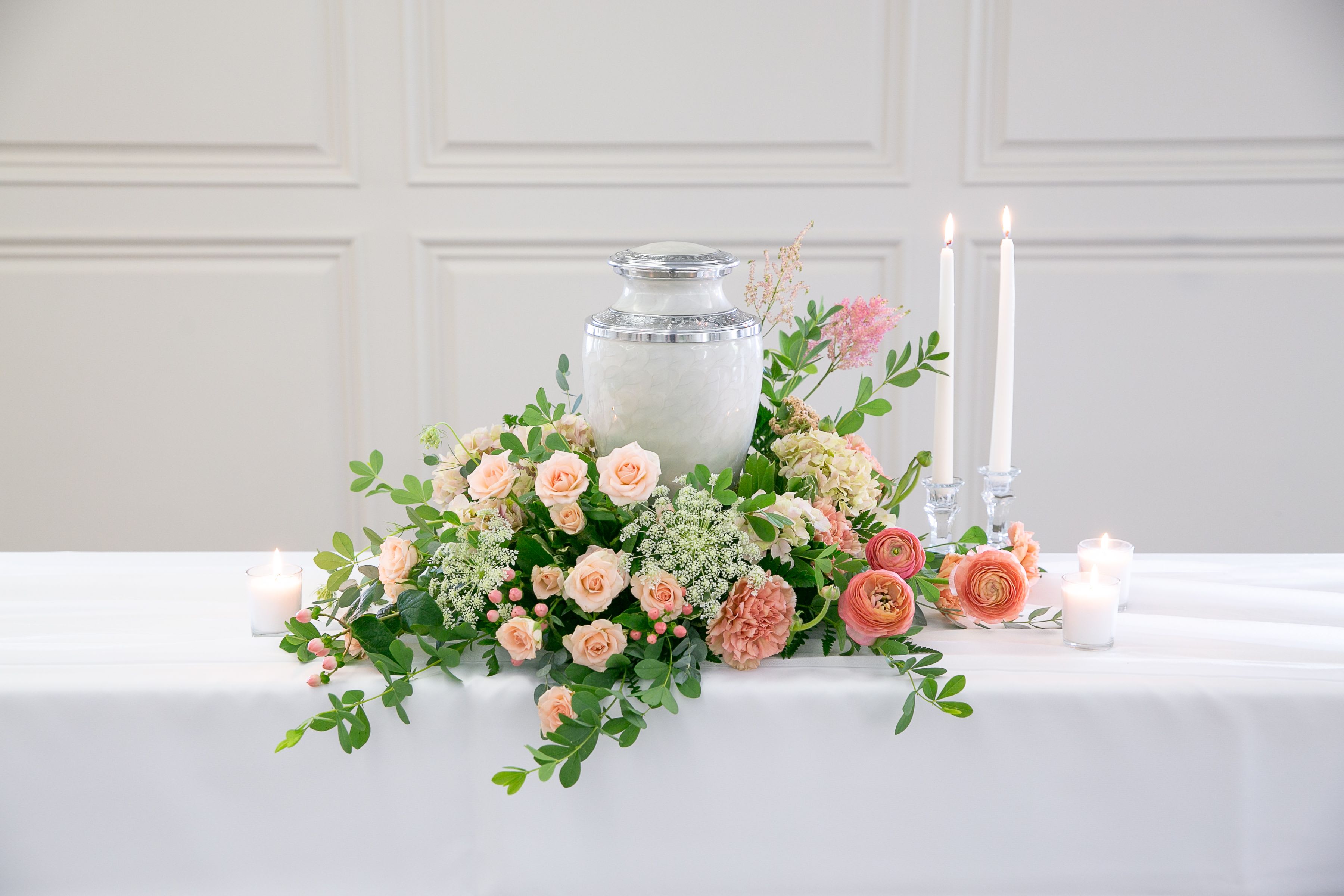 Blush Remembrance – Cremation Urn Wreath   - Soft, elegant, and filled with quiet grace, Blush Remembrance is a floral tribute designed to honor a life remembered with love.  This delicate urn wreath features a gentle blend of blush roses, peach ranunculus, soft carnations, and seasonal blooms accented with airy greenery and natural textures. The soothing palette of blush pink, soft peach, and fresh green creates a peaceful and comforting presence during moments of remembrance.  Designed in a low circular form surrounding the urn, the arrangement symbolizes eternity, love, and the enduring beauty of cherished memories. Its graceful garden style frames the memorial display while allowing the urn to remain the focal point.  Each tribute is handcrafted by the designers at ImpeKable Flowers in DeLand, using carefully selected seasonal blooms sourced from premium growers.  A meaningful floral expression for memorial services, celebration-of-life gatherings, or remembrance ceremonies.  Flower varieties may vary depending on seasonal availability while maintaining the same soft color palette and overall design style.