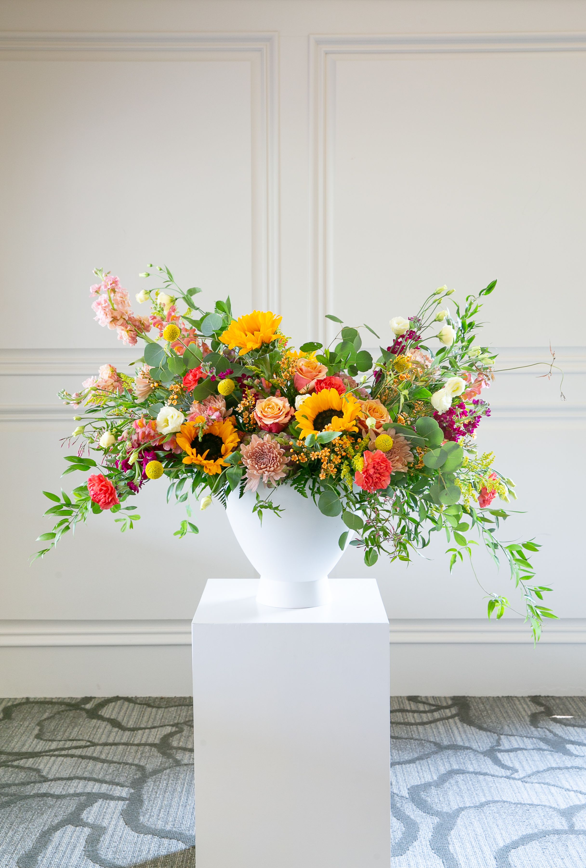 Wild Meadow – Garden Wildflower Arrangement - Bright, joyful, and naturally abundant, Wild Meadow captures the beauty of flowers gathered from a sunlit garden.  This vibrant arrangement features cheerful sunflowers, soft garden roses, seasonal blooms, and playful textural accents arranged with airy movement and fresh greenery. The warm palette of golden yellow, coral, peach, and soft pink creates a lively composition that feels organic, relaxed, and full of life.  Designed in a modern matte white vase, the arrangement blends the carefree charm of wildflowers with the refined touch of professional floral design. The natural movement of the blooms allows each flower to shine while creating a balanced, garden-inspired silhouette.  Each arrangement is handcrafted by the designers at ImpeKable Flowers in DeLand, using carefully selected seasonal blooms sourced from premium growers.  A beautiful choice for birthdays, celebrations, thank-you gifts, housewarmings, or sending a joyful surprise.  We proudly offer flower delivery throughout DeLand, Lake Mary, Sanford, Deltona, Orange City, DeBary, Altamonte Springs, and surrounding Central Florida communities.  Flower varieties may vary depending on seasonal availability while maintaining the same color palette and overall wildflower-inspired design style.