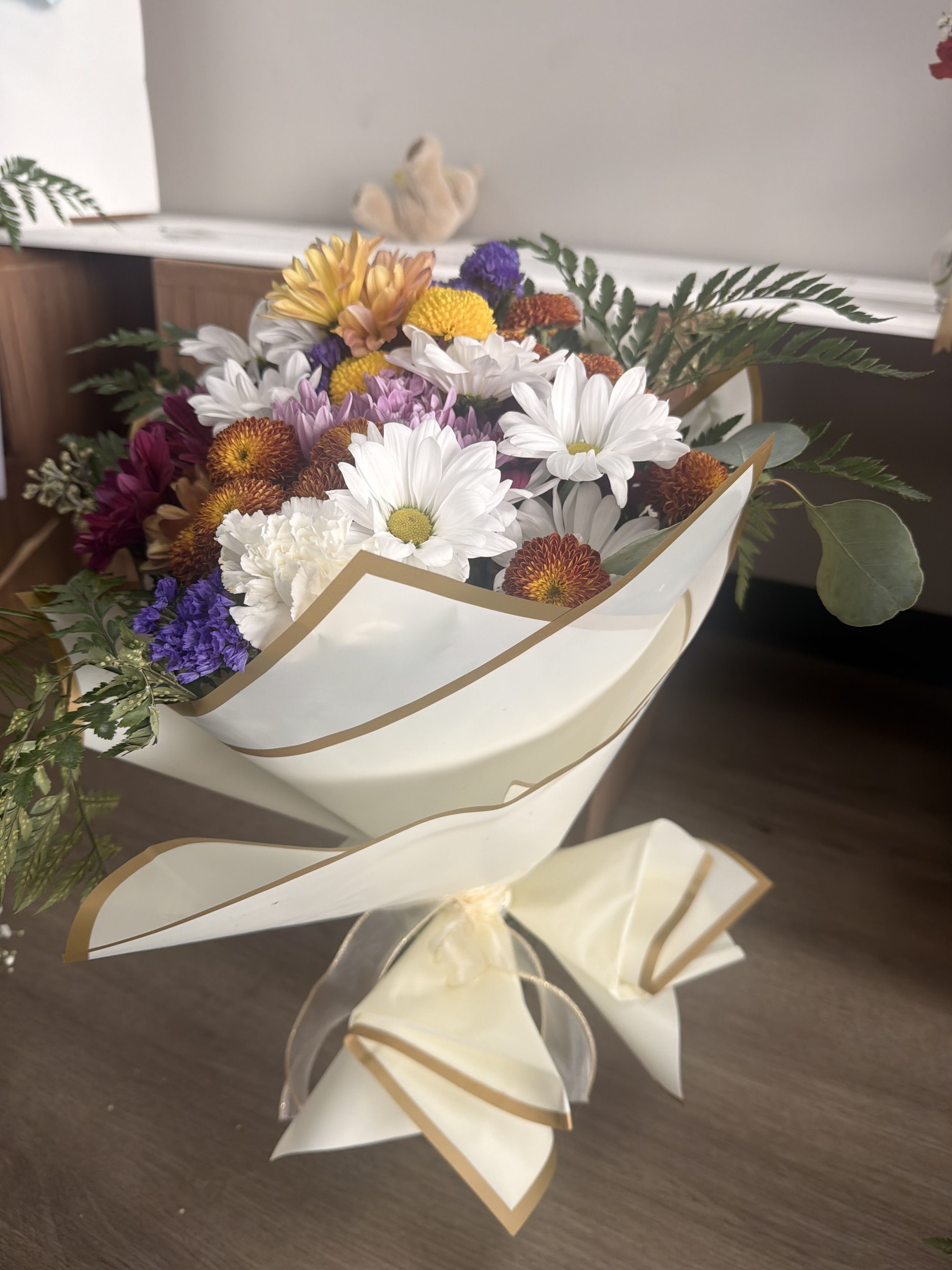 Bouquet of mixed daisies and chrysanthemums wrapped in cream paper