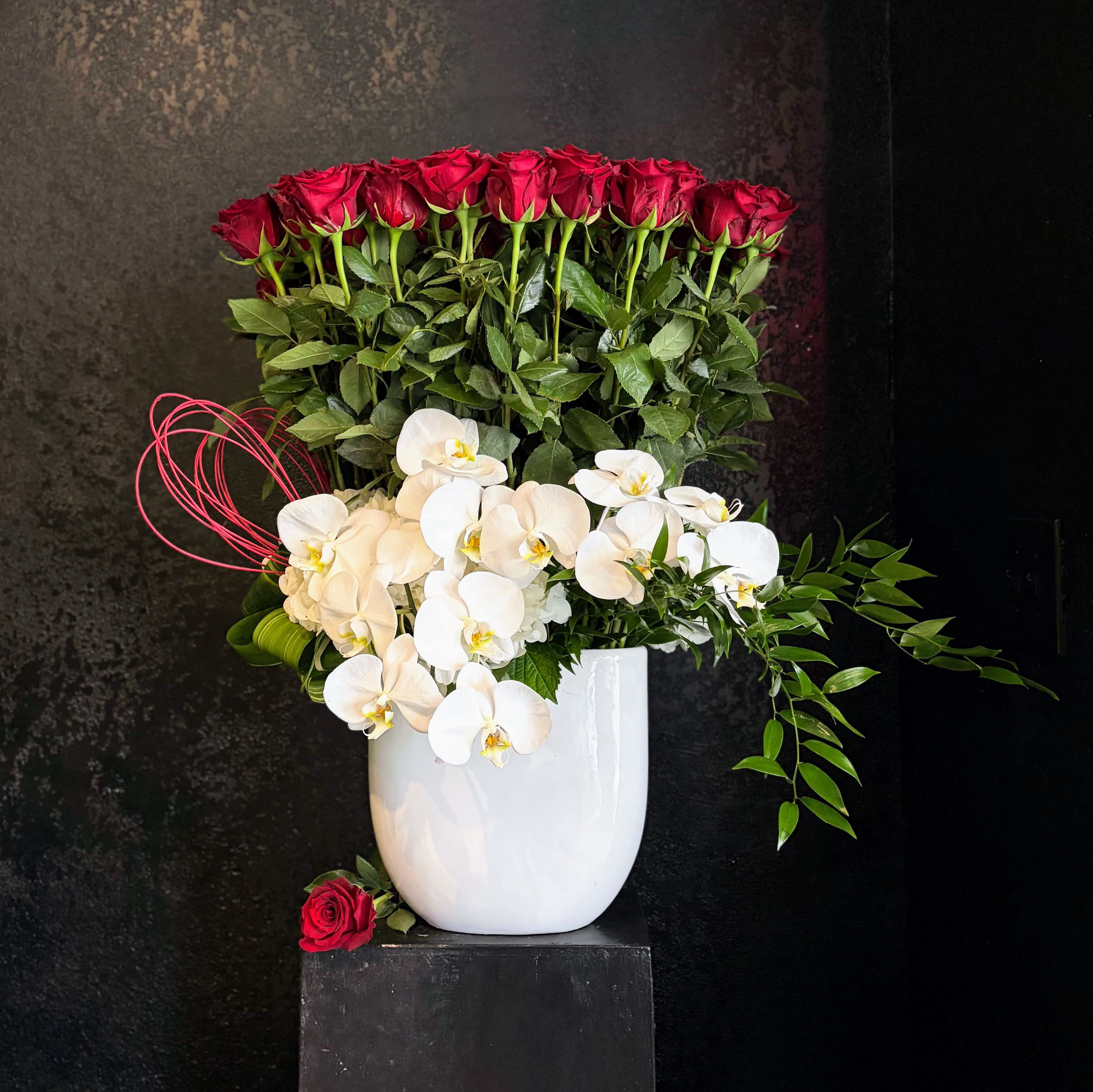 50 Ways - She's big.  She's beautiful.  She's FIFTY  Fifty long-stemmed red roses tower over a bed of pillowy hydrangea, leggy italian ruskus, and cascading orchids.