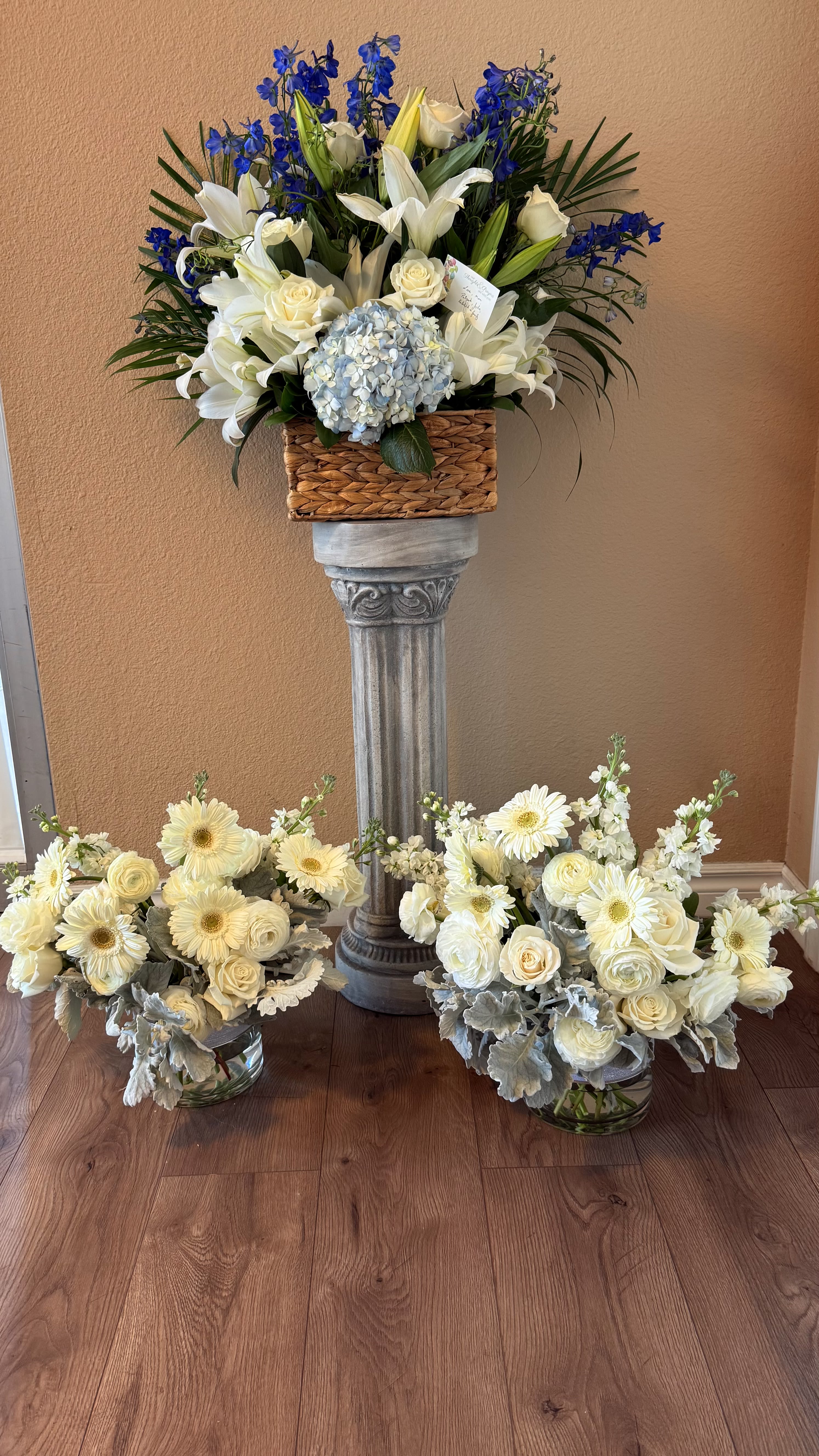 Heaven's Embrace Floral Tribute - Designed to bring comfort and serenity during moments of loss. Featuring elegant white lilies, roses, hydrangeas, gerbera, daisies, and soft greenery accented with touches of royal blue delphinium, this arrangements symbolize purity, grace, and eternal peace.