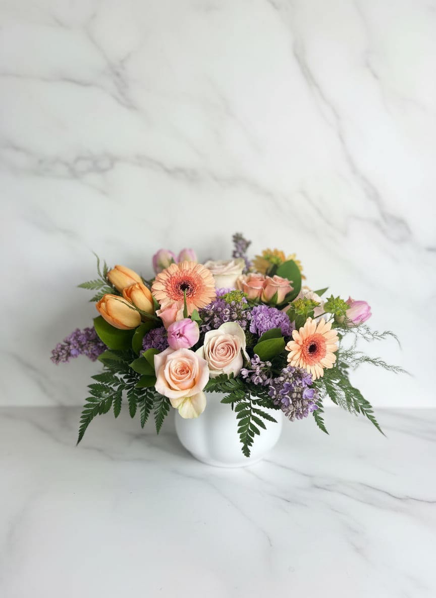 Breakfast in Bed  - This sumptuous and cheerful design is as welcome as a breakfast tray in bed. A collection of favorite spring blooms such as lilac, roses, and tulips overflow from a white scalloped container ( save to reuse for a potted plant afterwards! ) Aprox. 12x10 