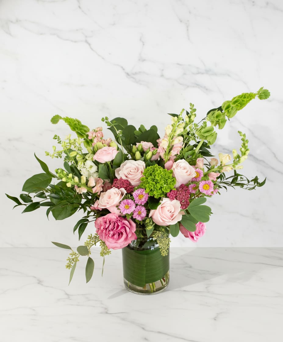 Arrangement of pink roses and mixed blooms with green hydrangea in a clear glass vase
