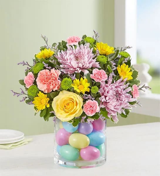 Easter Egg-Stravaganza - Our pastel bouquet brings fresh-picked spring beauty—and plenty of fun—into every home at Easter. Blooms are gathered in a clear glass cylinder vase filled with colorful plastic eggs for a uniquely playful touch.