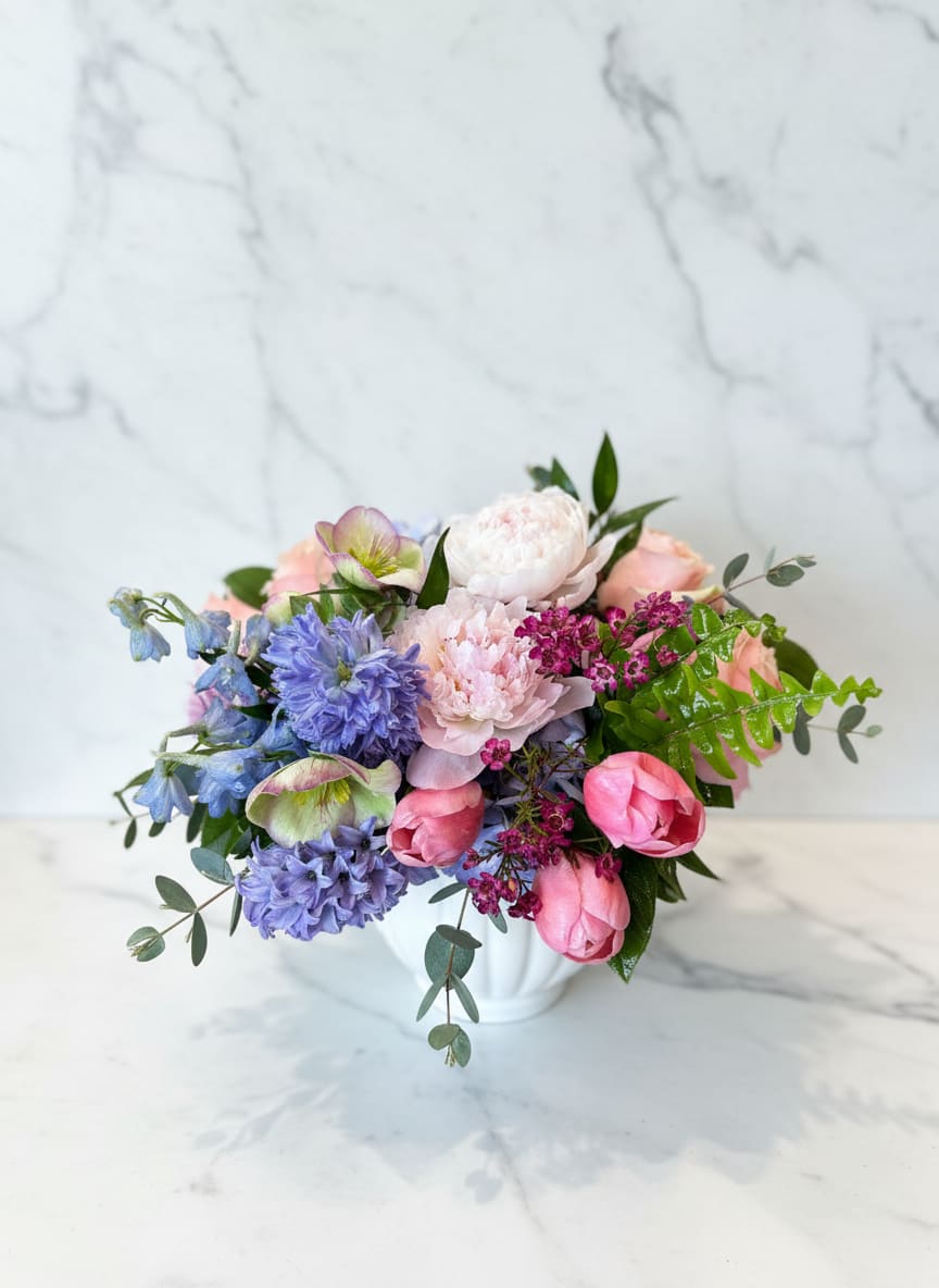 Spring Embrace  - A soft, garden-style arrangement gathered in fresh spring tones. Hydrangea, fragrant hyacinths and delicate roses are layered with airy accents in our fluted white ceramic container. Perfect for celebrating any loved one. 