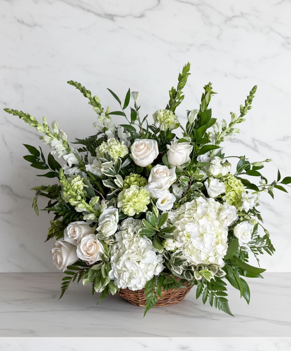 Sympathy Traditions  - Send your heartfelt sympathy - This traditional design is created in a natural wicker basket and is one of our most popular choices for flowers to send to the services.  We most often recommend a palette of whites, creams and greens, however we are happy to design a seasonal color palette as well.   Please call the shop for any specific needs.  Ribbon shown here as example - if you would like a customized ribbon banner please leave the details in notes.  Size shown is the deluxe, Approx. 15"x30"  **** We do not recommend this as a gift to a residence ***