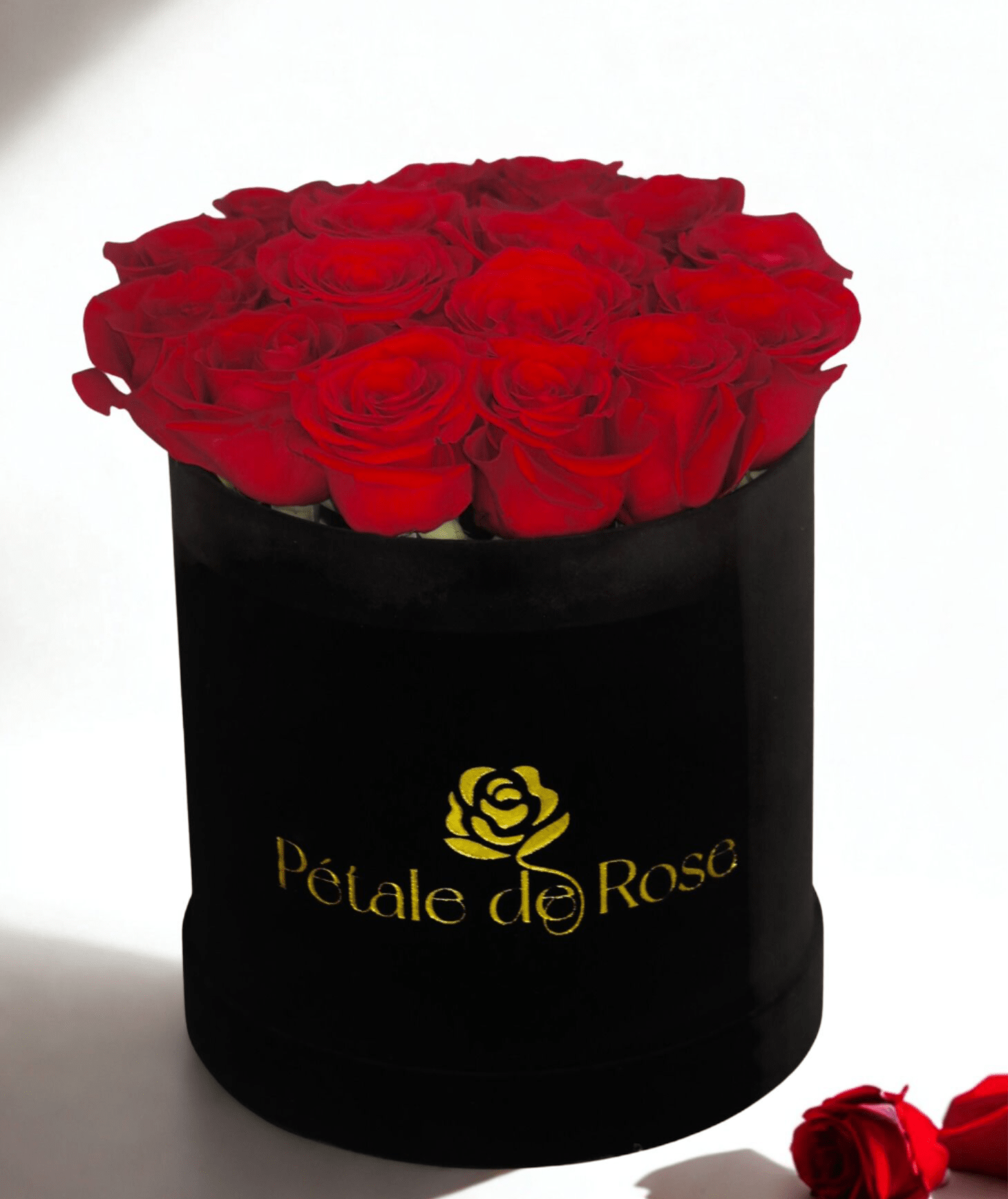 Round black hat box filled with tightly packed red roses with a gold logo on the front.