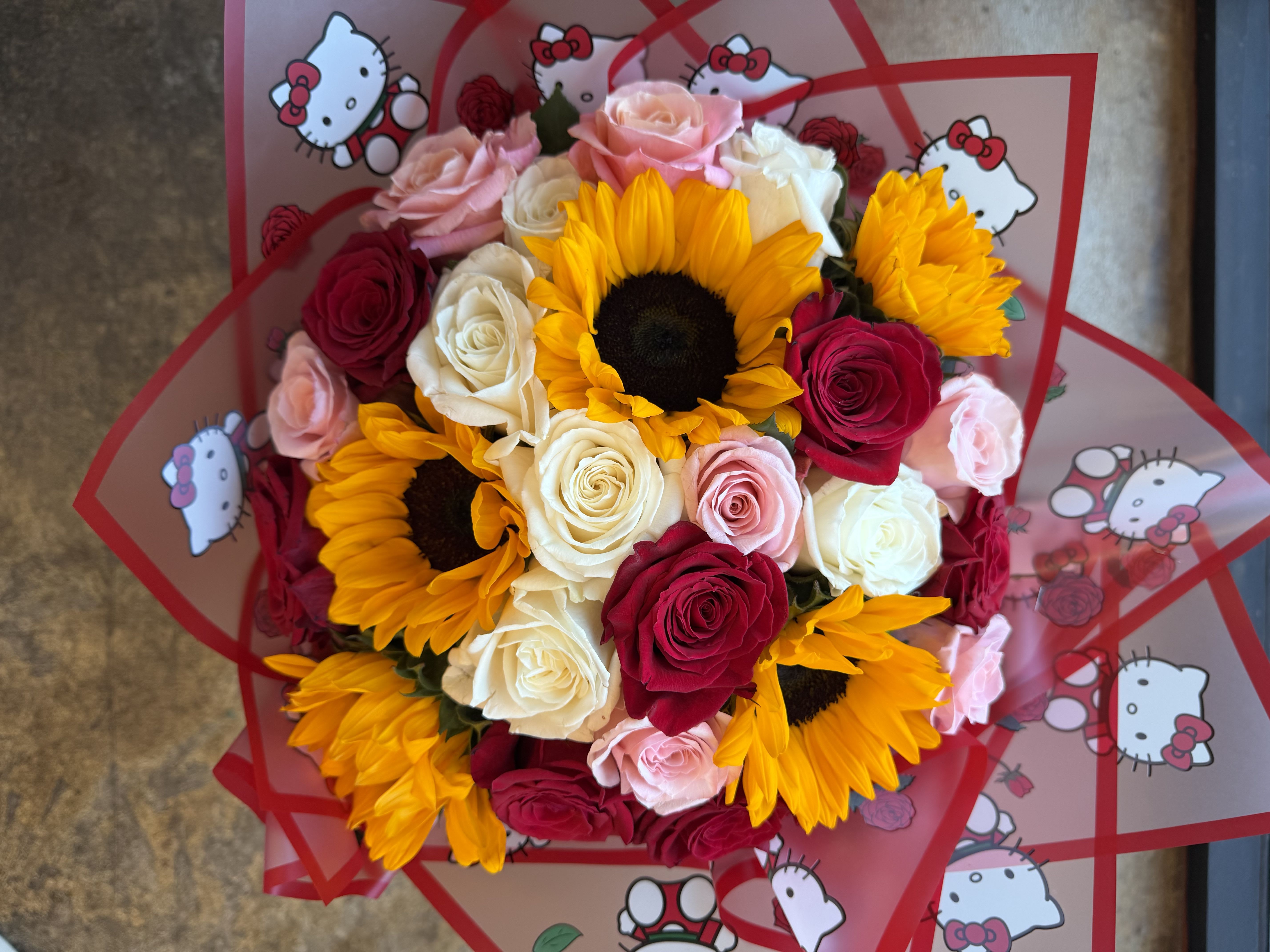 Hello Kitty Ramo Bouquet – Luxury Hand-Wrapped Rose &amp; Sunflower Arrangement Rancho Cucamonga - Bright, playful, and full of personality, our Hello Kitty Ramo Bouquet is designed to make a lasting impression. This eye-catching hand-wrapped arrangement features a stunning mix of red, pink, and white roses, paired with cheerful sunflowers and lush hydrangeas for a full, vibrant look.  Wrapped in adorable Hello Kitty-themed paper, this bouquet is perfect for birthdays, celebrations, graduations, or anyone who loves cute, stylish, and unique floral gifts. The Ramo-style presentation adds a modern, trendy touch that makes this arrangement feel extra special and gift-ready.  Each bouquet is carefully handcrafted by our floral designers, creating a beautiful balance of romance, fun, and elegance in every detail.  Available for same-day flower delivery in Rancho Cucamonga and throughout the Inland Empire, this one-of-a-kind bouquet is guaranteed to bring smiles and make any moment unforgettable.    Includes:  • Red Roses • Pink Roses • White Roses • Hydrangeas • Sunflowers • Hello Kitty Signature Wrap • Ramo-Style Handcrafted DesigN