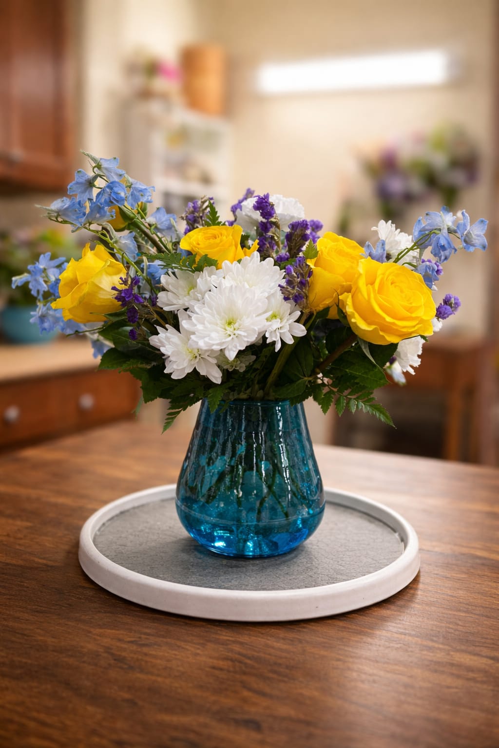 Sunshine breeze  - A cheerful mix of vibrant yellow roses, soft blue delphinium, and crisp white blooms arranged in a modern blue vase—perfect for brightening any space or gifting a touch of happiness.