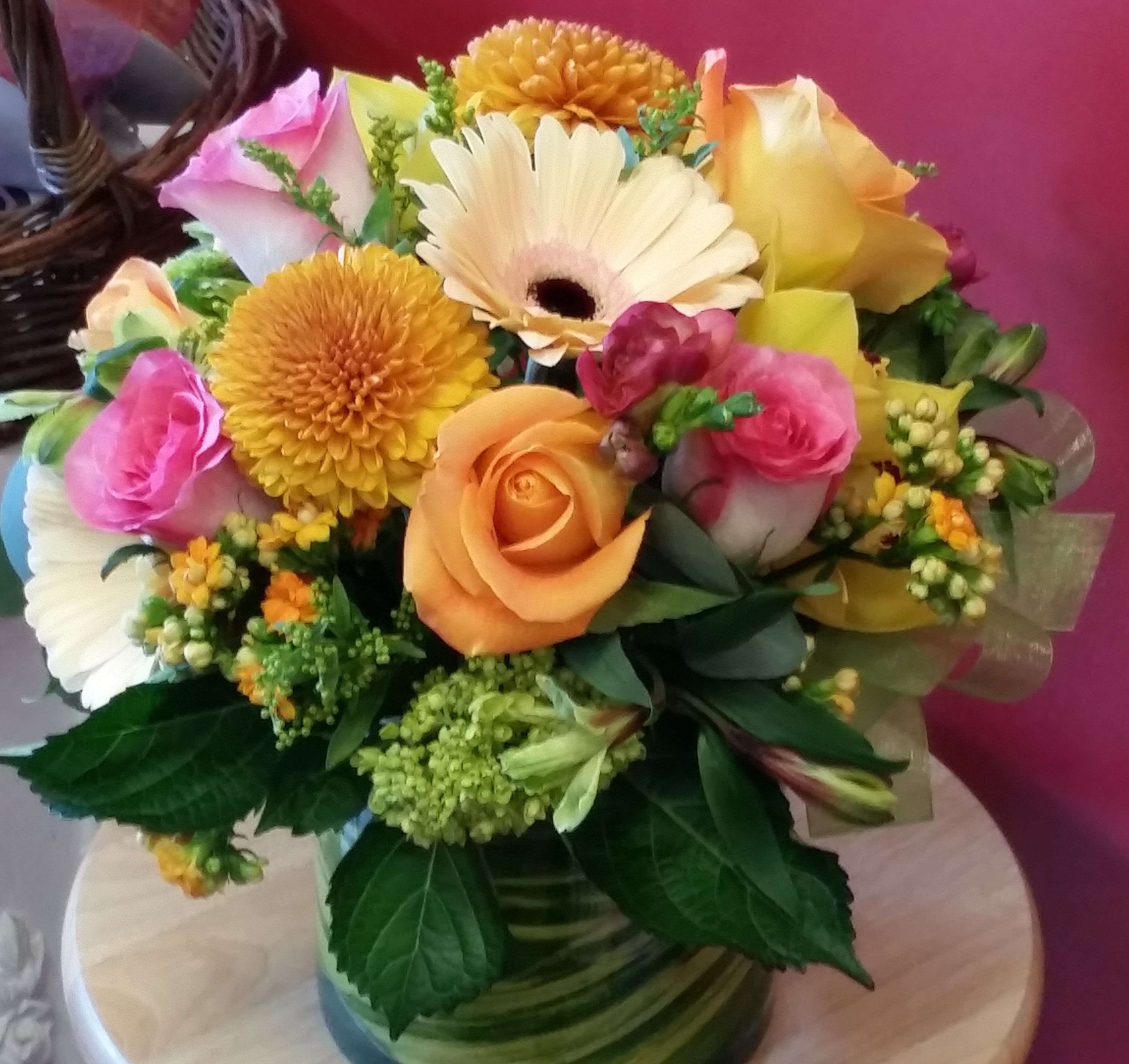 Color Splash - This enchanting selection of mid-range colored blossoms works for so many occasions.  Birthday, get well, anniversary, congratulations, thank-you.....this 5" diameter cylinder presents a collection of peach roses, green cymbidium orchids, golden chrysanthemum, and bright orange and pink accents.  A cheerful accent bow completes the picture for an all-around bright and cheerful arrangement.