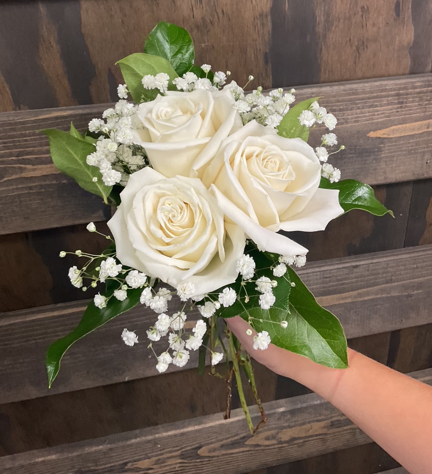 Marseille - Three roses gathered in a hand-tied nosegay create a compact, elegant prom bouquet that feels both timeless and fresh. The roses sit at the center so the person you're celebrating will look poised and photographed perfectly, while airy clusters of tiny white filler flowers soften the arrangement and add delicate texture. Looking for a color other than white?  Select yellow, orange, pink, red or lavender by requesting it in special instructions during check out.  Deep green foliage frames the blooms and extends just beyond the petals for a clean silhouette that's easy to hold. This petite arrangement is ideal for prom, small ceremonies &amp; romantic gestures- it's the kind of bouquet that makes someone feel seen and special.   Pickup dates for prom are Saturday, April 11th, 18th, 25th and May 2nd; please call if you need this for a different date.