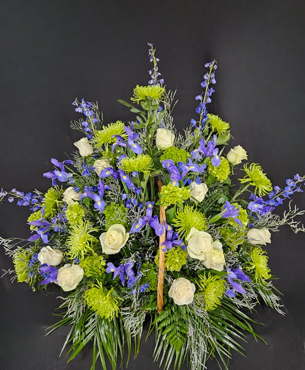 Peace &amp; Serenity Fireside Basket - May you find peace and serenity in your eternal rest. This elegant fireside basket combines hues of blue and green including Iris (when seasonally available), delphinium, limonium, hydrangeas, fuji mums, and trick with beautiful white roses. The basket is a woven wood and measures 2 feet long by 1.5 feet wide. Actual arrangement reaches out beyond this for a fuller, more impressive display.