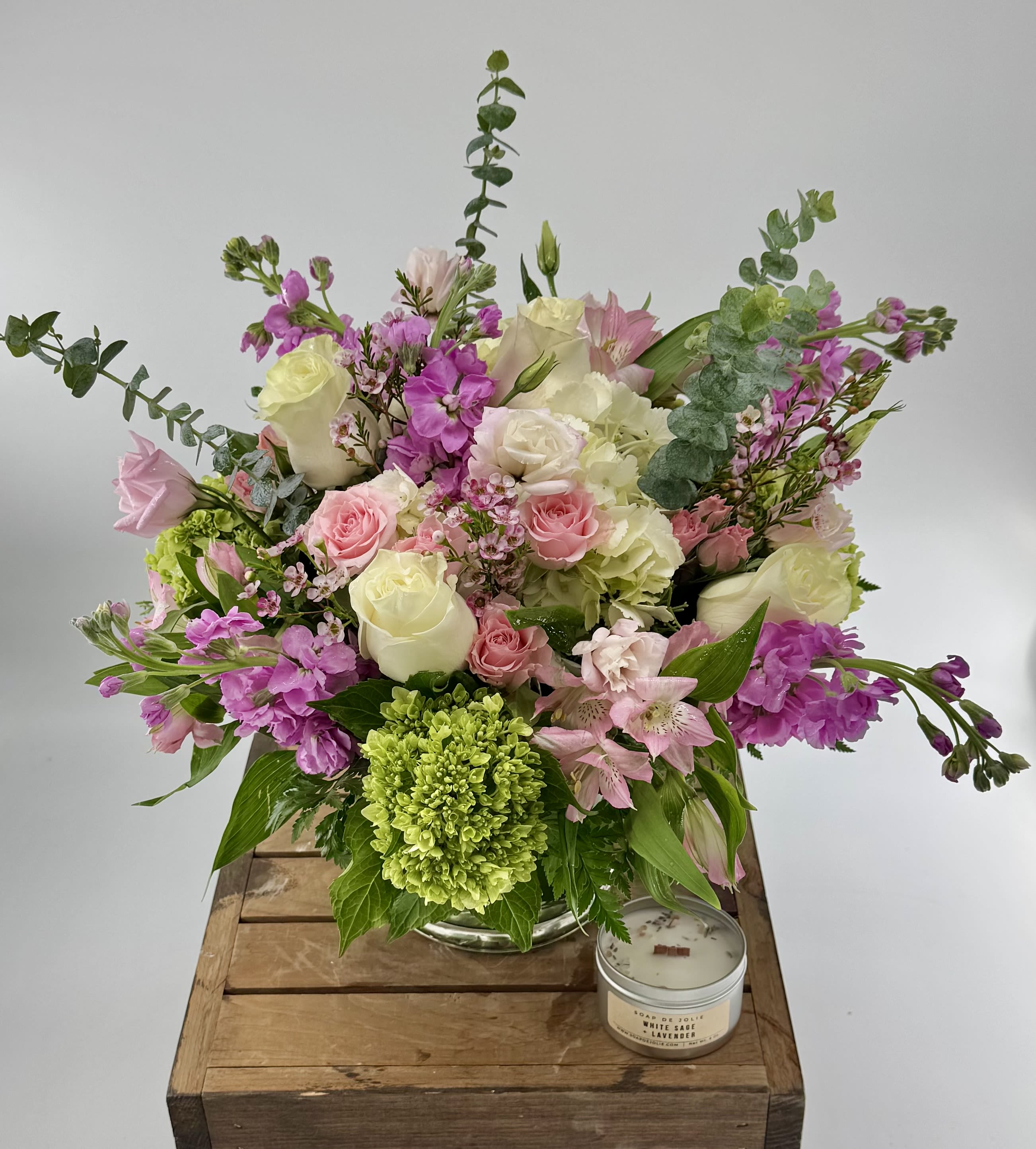 Pink and white mixed flower arrangement in a glass vase with a green bloom and a small candle beside it