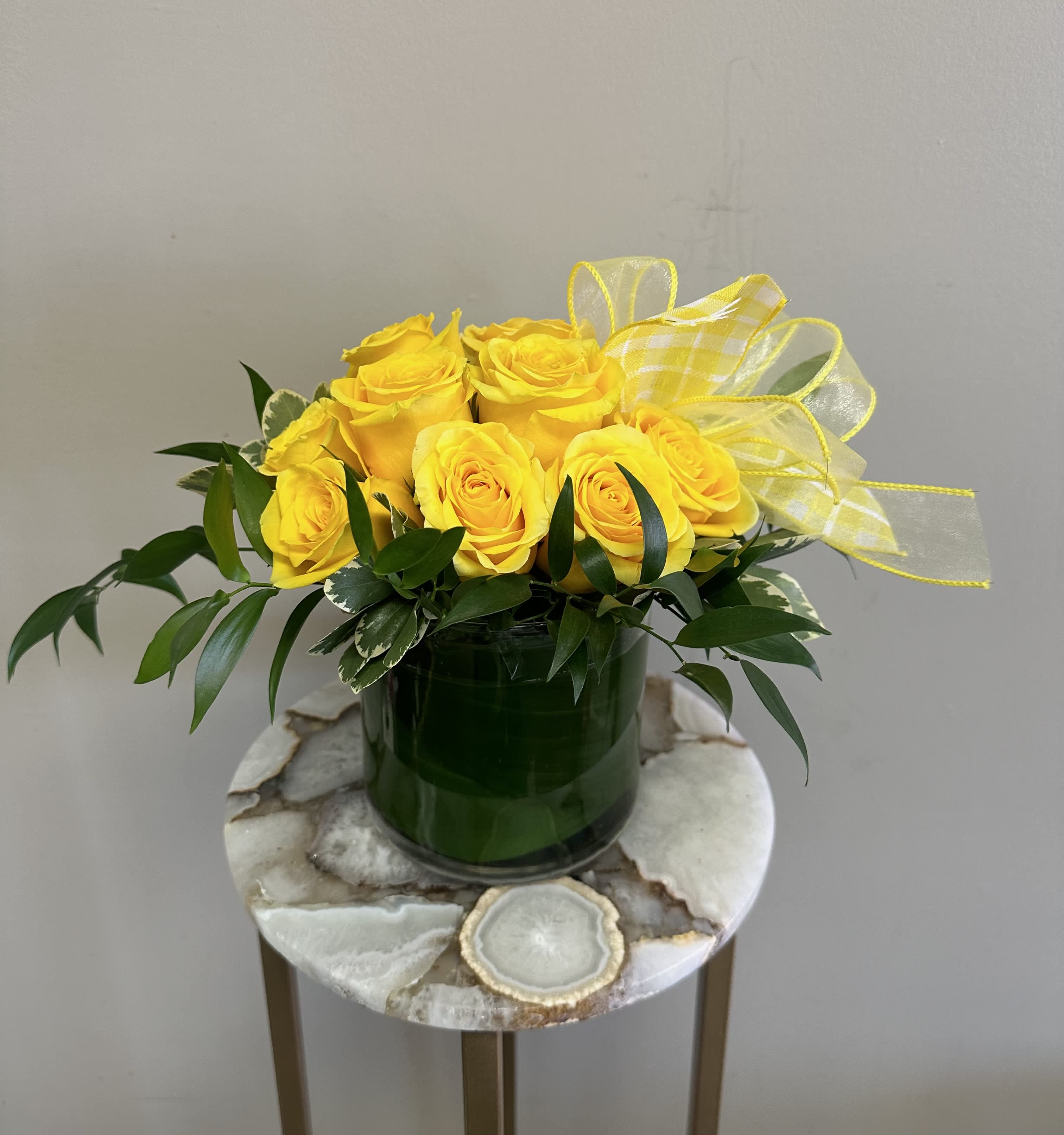 Sunny Side Up - A dozen yellow roses in a modern styled shorter vase with greenery around the sides. These roses are the perfect gift for anniversaries, birthdays, retirement, or even just because! Order for a same day or next day delivery and give us a call if you want custom flowers. 