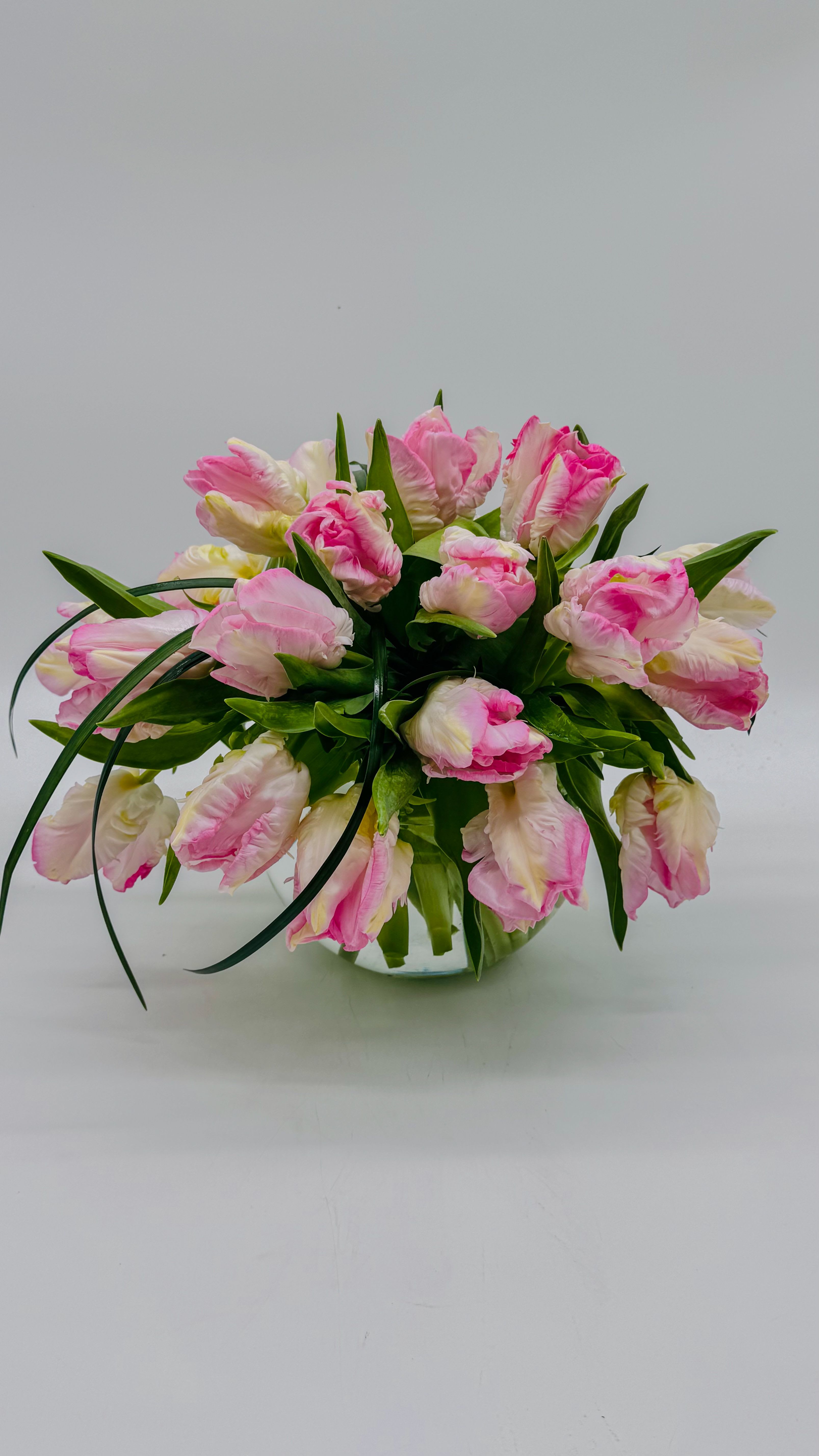Dutch Tulips  - A lush dome of ruffled parrot tulips-soft blush pinks mixed with creamy whites-creates an instantly romantic spring centerpiece perfect for a birthday bouquet, anniversary roses alternative, or a cheerful get-well gift. This low, relaxed table arrangement gives the person you're thinking of a fresh, joyful impression: the arching petals and lively textures read intimate and celebratory without feeling fussy.  Arranged tight and outward in a clear glass bowl vase, the Dutch Tulips design forms a dense, cascading cluster that sits low on the table and invites close-up appreciation of each frilled petal. The parrot tulips' ruffled edges and the gentle pink-to-white palette bring both movement and softness, while the glass bowl highlights the short, neat stems for a clean, modern look.  Perfect for personal celebrations, everyday brightening, or a thoughtful surprise that says "I'm thinking of you," this arrangement is ready to place on a dining table, desk, or bedside. Care is simple: keep stems trimmed, change the water regularly, and display away from direct heat to prolong the fresh, springlike bloom.