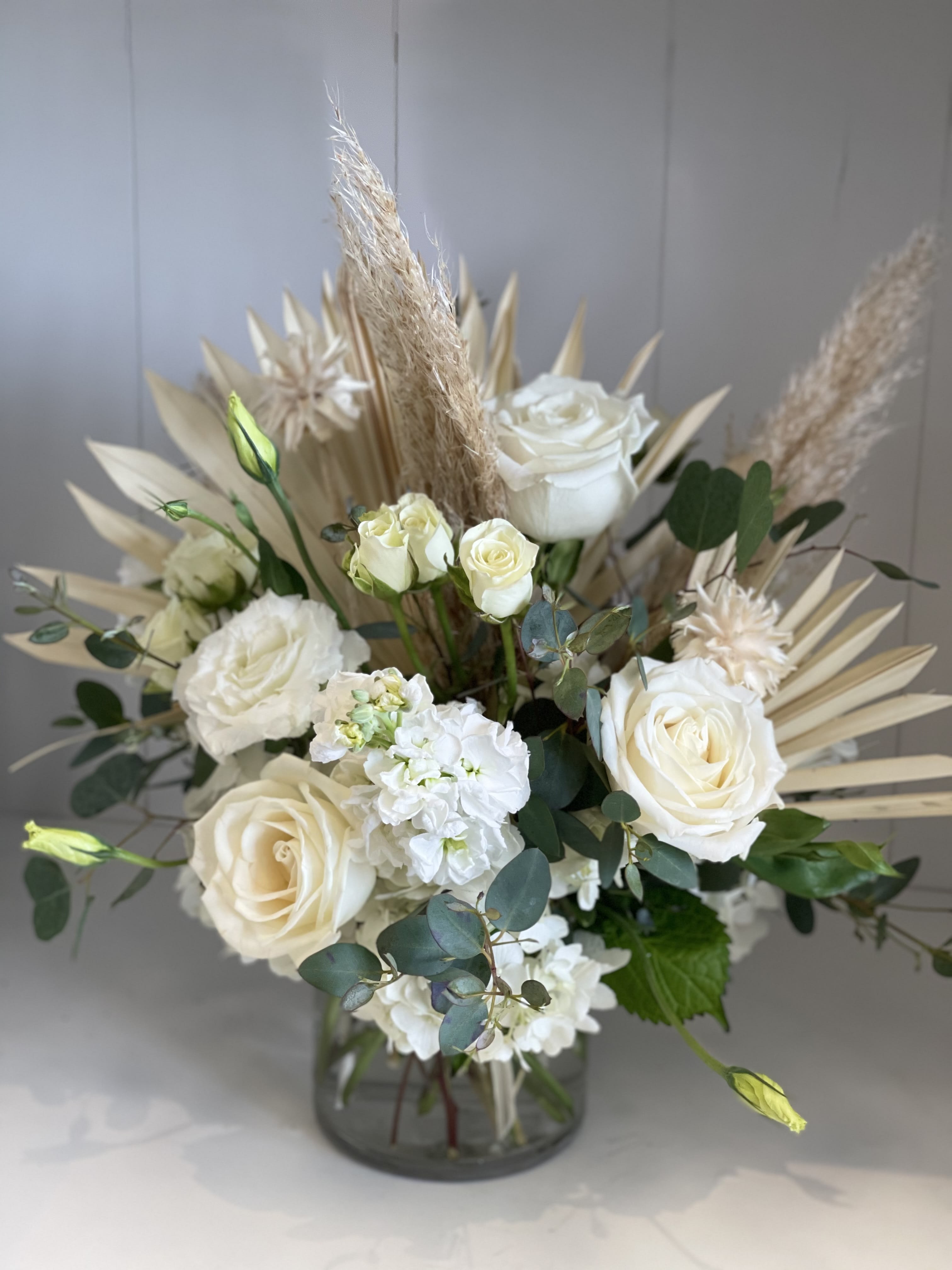 Starlight - A beautifully soft and elegant arrangement in delicate shades of cream and white, featuring classic roses, spray roses, and lush hydrangeas, complemented by unique dry elements for added texture and charm. This timeless design exudes serenity and sophistication, making it perfect for any occasion.  