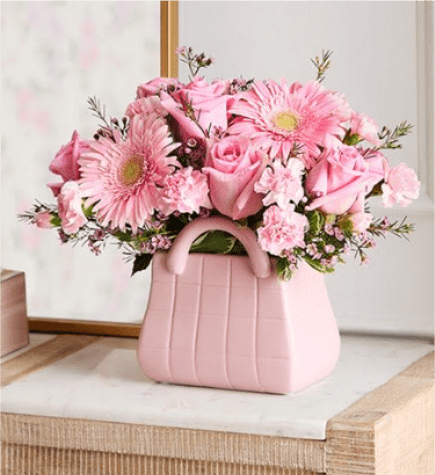 Designer Dreams™ Bouquet (ceramic Bag) - NEW The ultimate arrangement for your favorite fashionista. A profusion of roses, poms, and other blooms all but spill out of the top of our keepsake handbag-shape vase, making this a truly chic gift. And just like the perfect handbag, the pink, white, and lavender bouquet goes with just about everything. More details  Arrangement of pink roses and mini carnations, white button poms, lavender daisy poms, purple limonium, and foliage