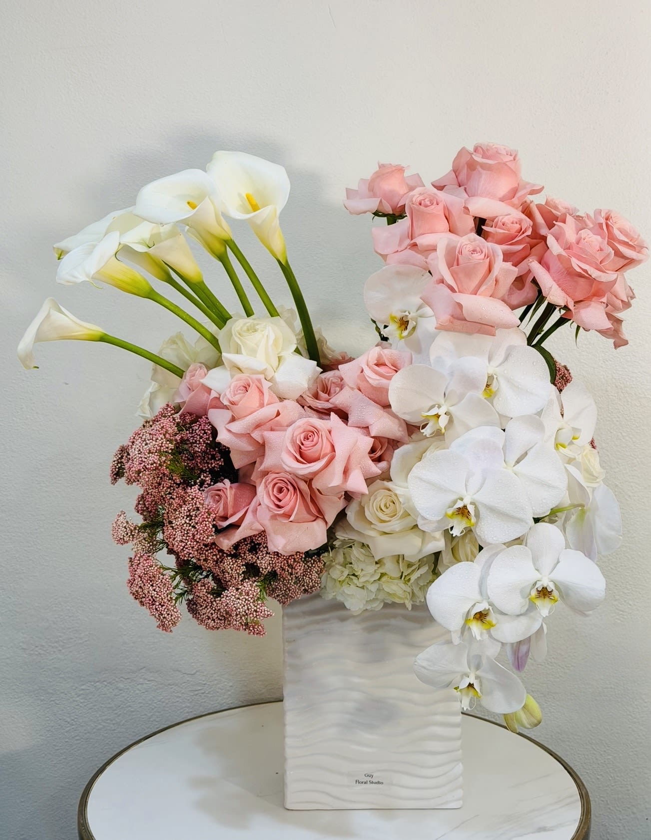 Blush Orchid Elegance - Experience refined elegance with our Blush Orchid Elegance, a luxurious floral arrangement designed in soft blush pink and crisp white tones. Featuring premium roses, graceful phalaenopsis orchids, and elegant calla lilies, this arrangement is thoughtfully composed to create a sophisticated and timeless look. The delicate balance of textures and colors brings a sense of calm beauty and modern luxury, making it perfect for birthdays, anniversaries, romantic gestures, or any special occasion. Designed in a sleek contemporary vase, this piece makes a stunning statement in any home or space. Each arrangement is handcrafted at Guy Floral Studio with exceptional attention to detail and the highest quality blooms. We proudly offer same day flower delivery in West Hollywood, Beverly Hills, Bel Air, Beverly Grove, Santa Monica, Culver City, Hollywood Hills, Hollywood, and surrounding Los Angeles areas.
