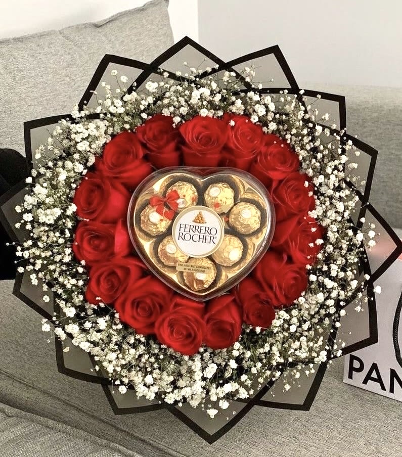 Round bouquet of red roses and white filler flowers with a heart box of chocolates in the center