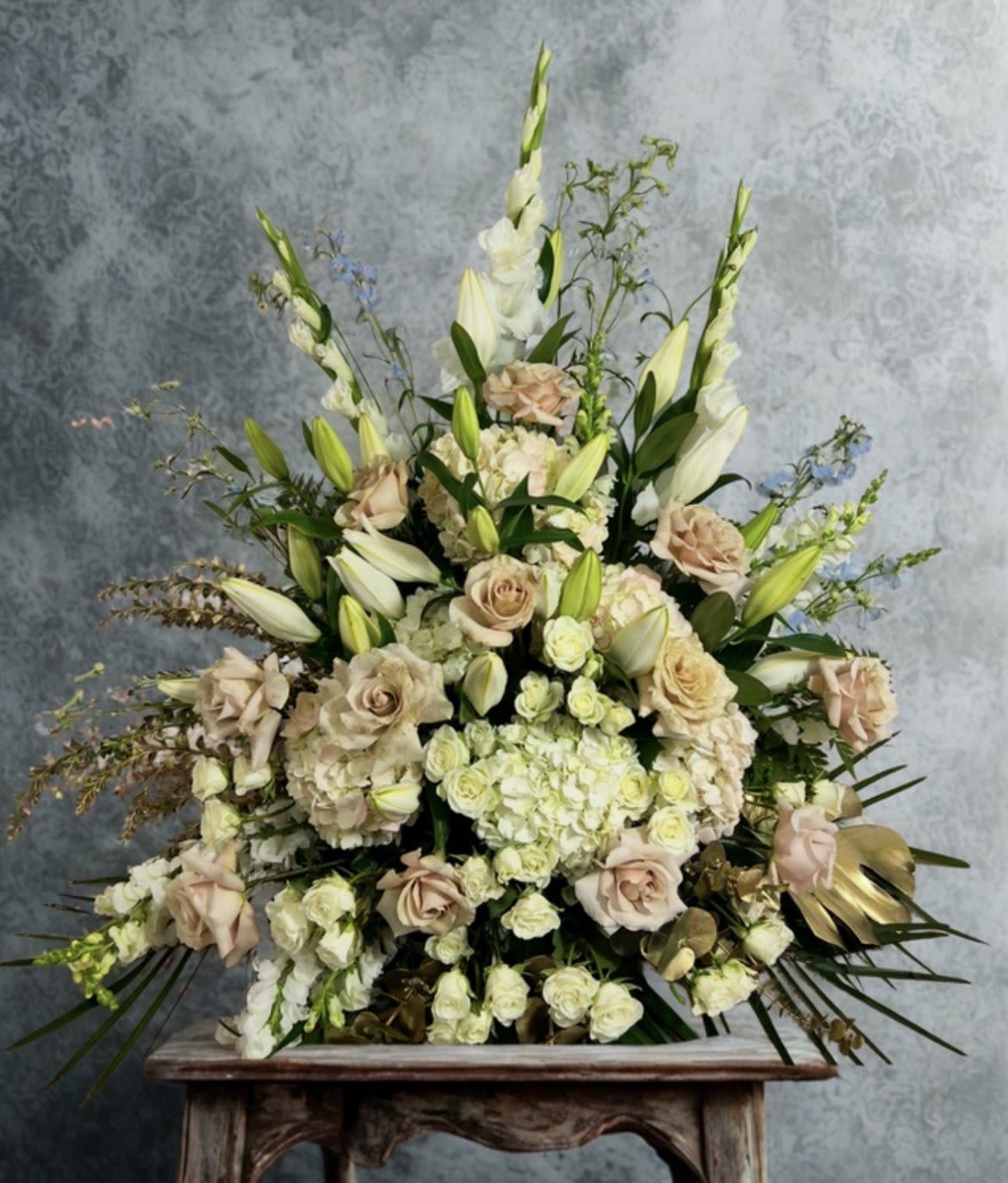 Champagne Elegance - A refined and romantic display featuring soft quicksand roses, creamy white lilies, spray roses, gladiolus and lush hydrangeas. Accented with delicate fillers, golden foliage, and touches of greenery, this arrangement radiates timeless beauty—perfect for weddings, ceremonies, or sophisticated celebrations.
