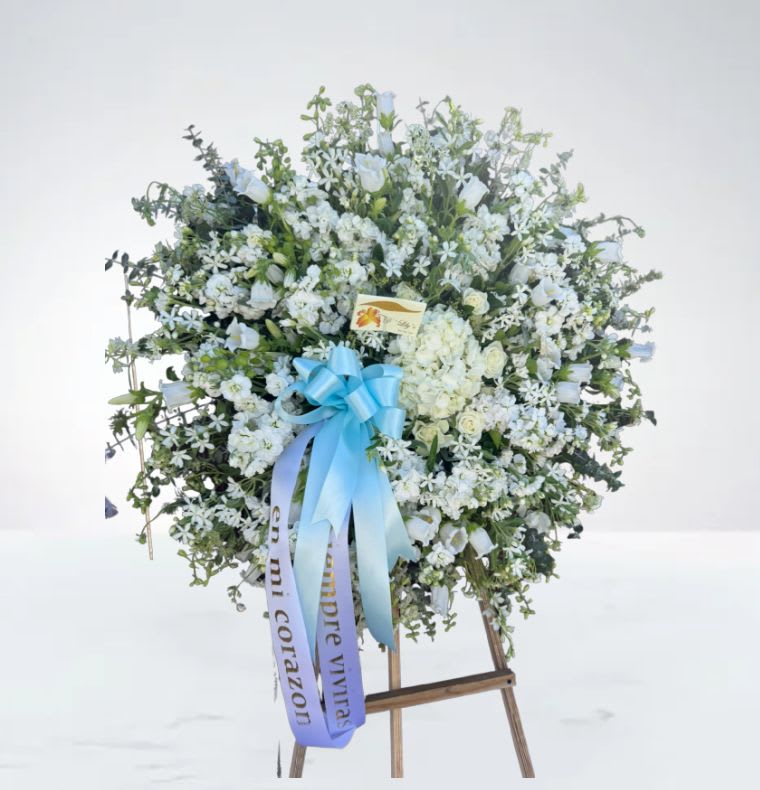 Peaceful Remembrance Wreath  - A soft and elegant wreath made with white and touches of blue flowers. A beautiful way to say goodbye and honor someone’s memory with love and respect. 