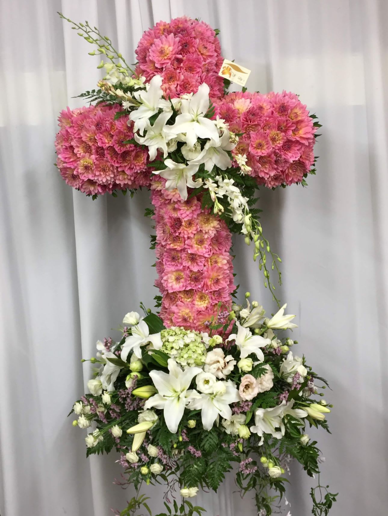 Heavenly Grace Cross - This stunning cross is made with radiant dahlias, pure white lilies, dainty lisianthus, cheerful daisies, and cascading orchids. This floral tribute speaks of everlasting life, beauty, and unwavering faith.