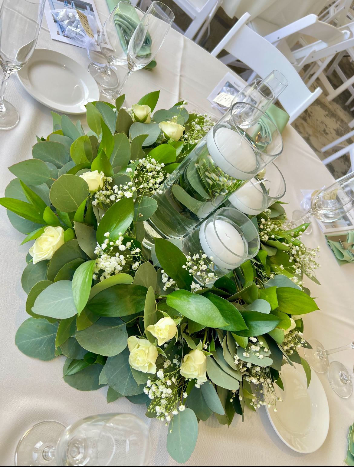 Eucalyptus Elegance Centerpiece  - A stunning blend of eucalyptus, crimson blooms, and floating candles, creating a warm and elegant atmosphere for any special occasion.  DISCLAIMER: 3 Vase rental only.  Wreath and candles available to keep.  