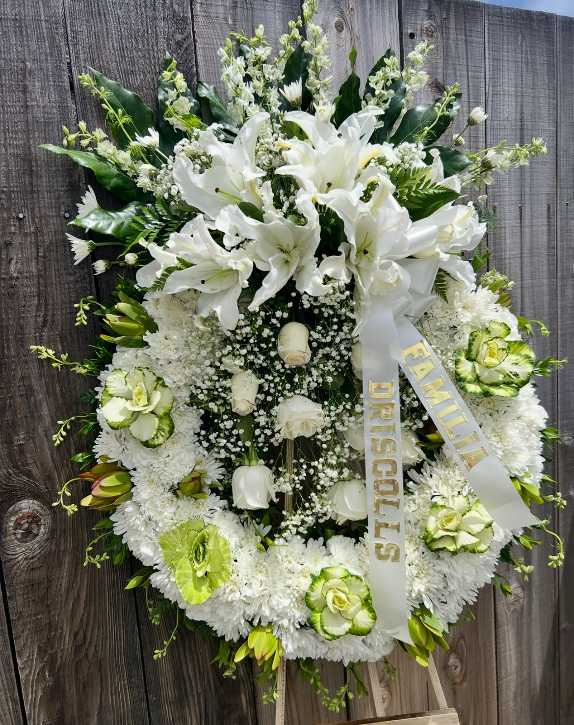Angelic Tribute - A serene expression of sympathy, this elegant wreath features white lilies, roses, and chrysanthemums, accented with soft greens. Designed to honor a life with grace and love, it offers comfort and remembrance to grieving hearts.