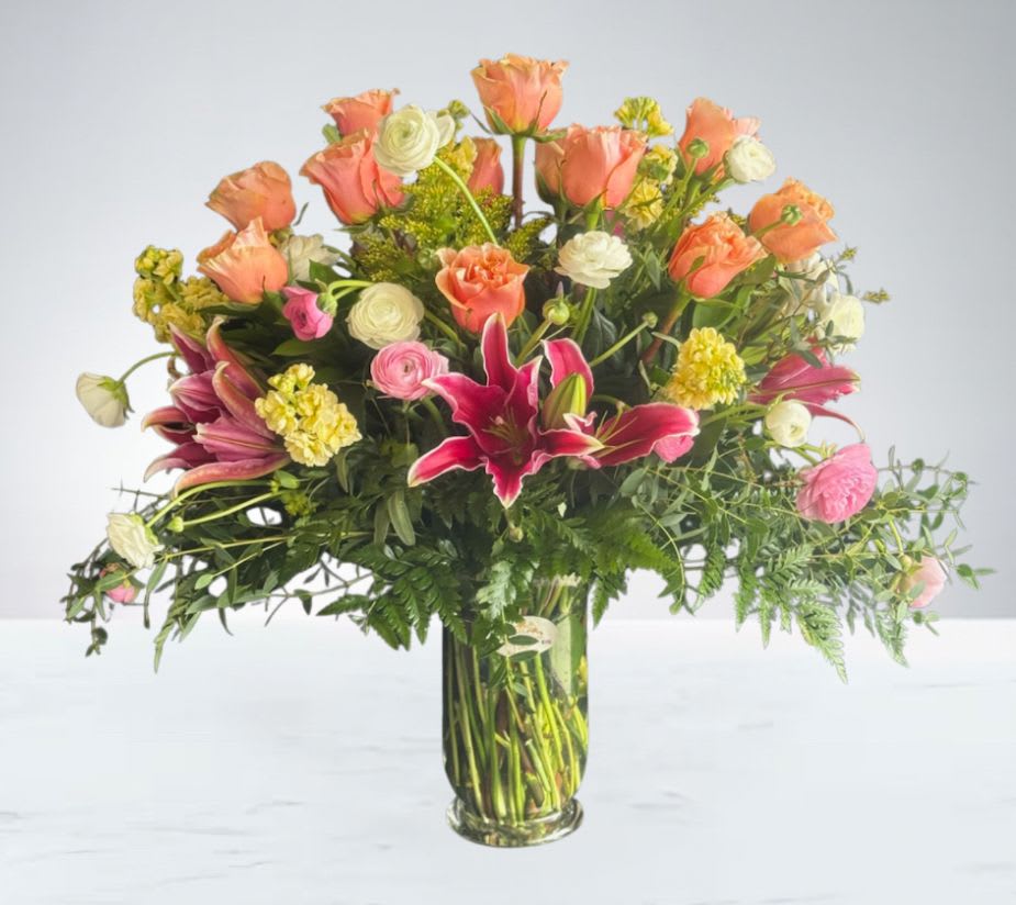 Lush &amp; Lovely by D'Lily's Flowers  - A vibrant mix of coral roses, stargazer lilies, and delicate blooms arranged in a glass vase. This cheerful bouquet brings warmth, beauty, and joy to any space.