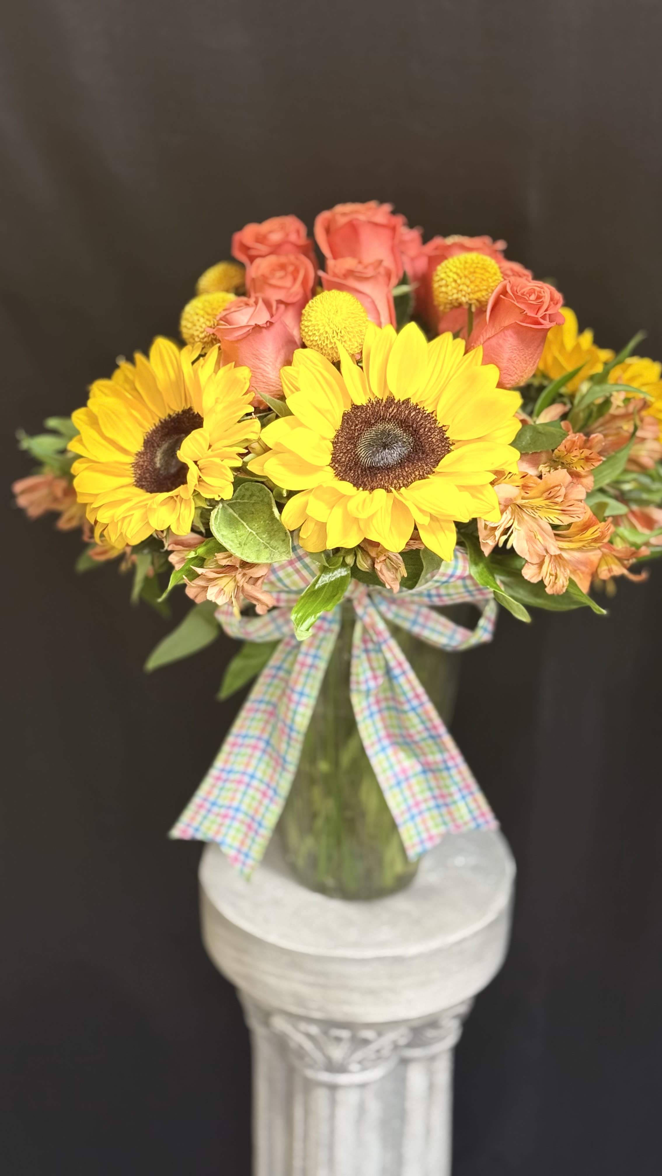 Sunny Delight - Bursting with cheer, this radiant arrangement combines golden sunflower, orange roses, and playful yellow billy balls, accented with soft alstroemeria and lush greenery. Finished with pastel plaid bow, it"s a joyful design that brings warmth, happiness, and sunshine into any space_perfect for celebration life's bright moments!