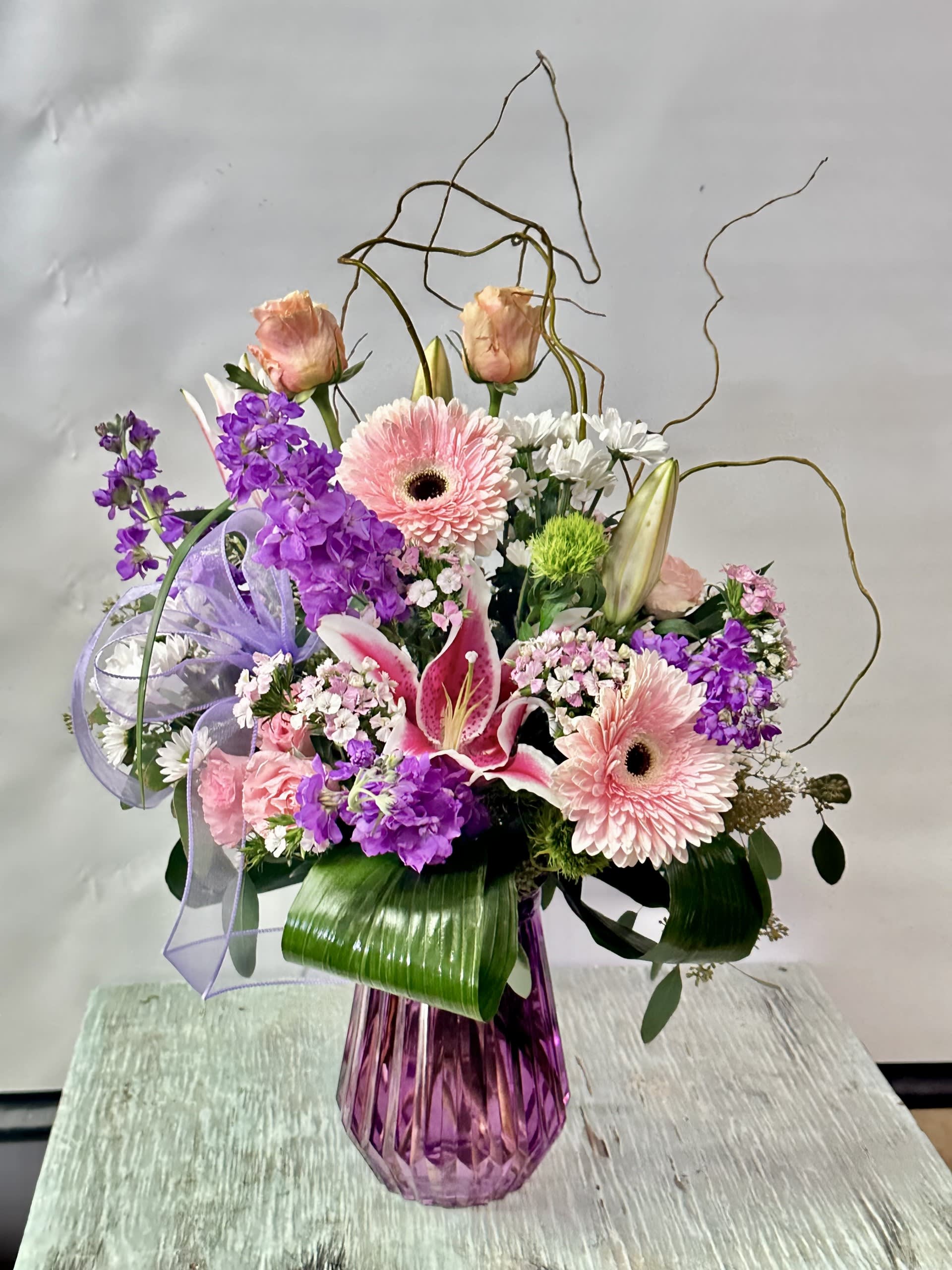 Anniversary #9 - Arrangement of pink, purple and white flowers in a purple glass vase. Adorned with a lavender bow.