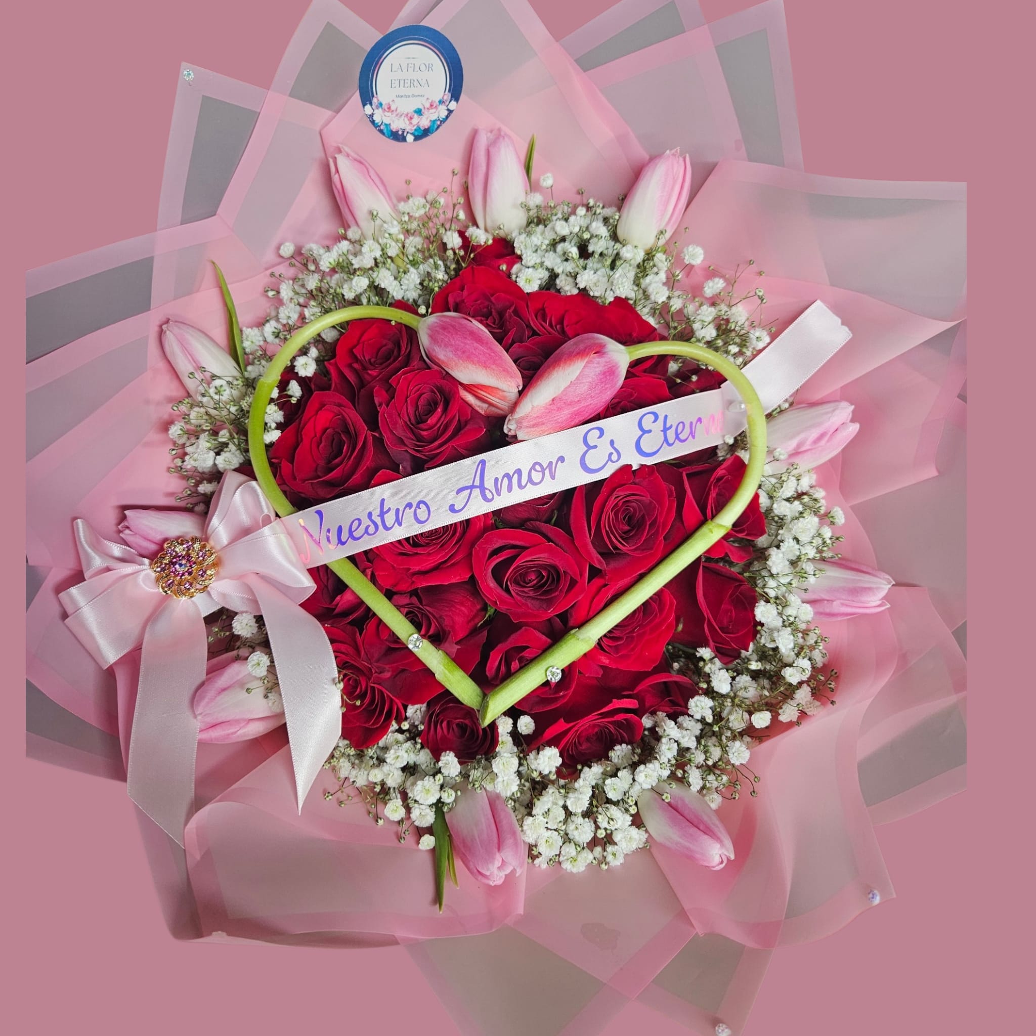 Roses &amp; tulips Garden - A lush ring of velvety red roses forms the heart of this romantic flower arrangement, perfect as an anniversary bouquet or Valentine's Day gift  Soft pink tulips cradle the roses in a gentle outer circle while delicate white filler flowers add a light, airy contrast-together they create a classic, sentimental look that makes the recipient feel deeply cherished.  The arrangement is wrapped in layered pink floral paper and finished with a large pink satin ribbon bow accented by a jeweled brooch and a printed message ribbon across a green heart-shaped frame laid over the roses. Two tulip buds rest at the top of the heart for an intimate, bespoke touch; a round brand tag and a heart-shaped decorative frame complete the presentation. This piece balances rich reds and soft pinks with fresh greenery for a visually striking, tactile bouquet.  Ideal for celebrating anniversaries, Valentine's Day, or a meaningful personal gesture, this design reads as both romantic and celebratory-the kind of gift that makes someone feel truly seen and adored. Order with standard sizing; keep flowers in fresh water and trim stems every few days to extend their display.