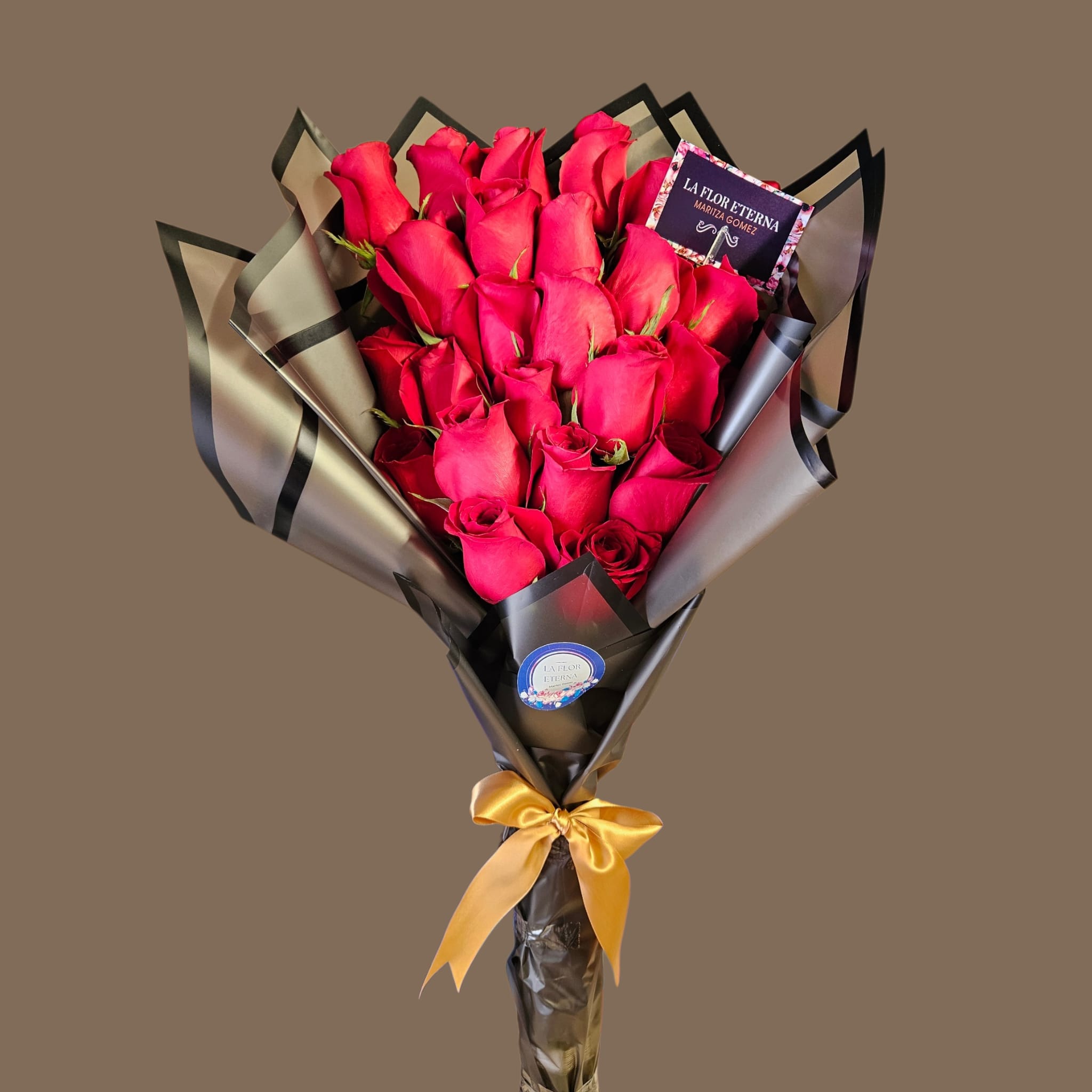 Luxury Love  - A dense cluster of vivid red roses-arranged upright in a tight, sculpted bouquet-creates a boldly romantic statement perfect for an anniversary or Valentine's Day gift. The vivid red petals pop against layered black and translucent cellophane wrap, whose sharp, angular edges give the design a modern, dramatic silhouette; the finished look reads luxe and intentional, ideal for the person you're celebrating.  Each bouquet is finished with decorative paper, a gold satin ribbon bow at the base, and a small printed card tucked into the blooms for your message. The compact, upright arrangement emphasizes rich color and texture-soft velvety roses framed by structured wrap-so she'll feel truly seen and adored when it arrives. Order with delivery notes for timely arrival; stems are arranged for vase-ready display so minimal care is needed beyond fresh water and a cool spot away from direct sunlight.