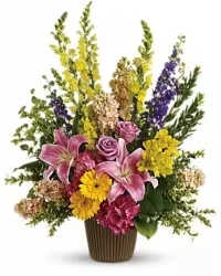 GRACEFUL FLOOR BASKET  - A tall, fan-shaped floor basket that greets the room with a burst of sunny energy-this flower arrangement is a graceful floor basket perfect for a birthday bouquet, get well wishes, or a colorful sympathy gift. The composition places pink lilies and roses at the heart, so the person you're thinking of will feel both cherished and uplifted; bright yellow gerbera daisies and vertical yellow flower spikes lift the design and add cheerful height.  Close-up, the arrangement pairs soft pink lilies and roses with pink carnations, purple delphinium, and snapdragons for texture and movement, while mixed bouquet elements fill the base for a full, abundant look. Housed in a ribbed brown ceramic vase, the piece reads classic and grounded; the mixed color palette of yellow, pink, and purple keeps the mood energetic without being overbearing. Sized as a substantial floor basket, it makes a statement in entryways, hospital rooms, or beside a memorial display-order with confidence knowing it's arranged to arrive fresh and arranged to comfort and celebrate.