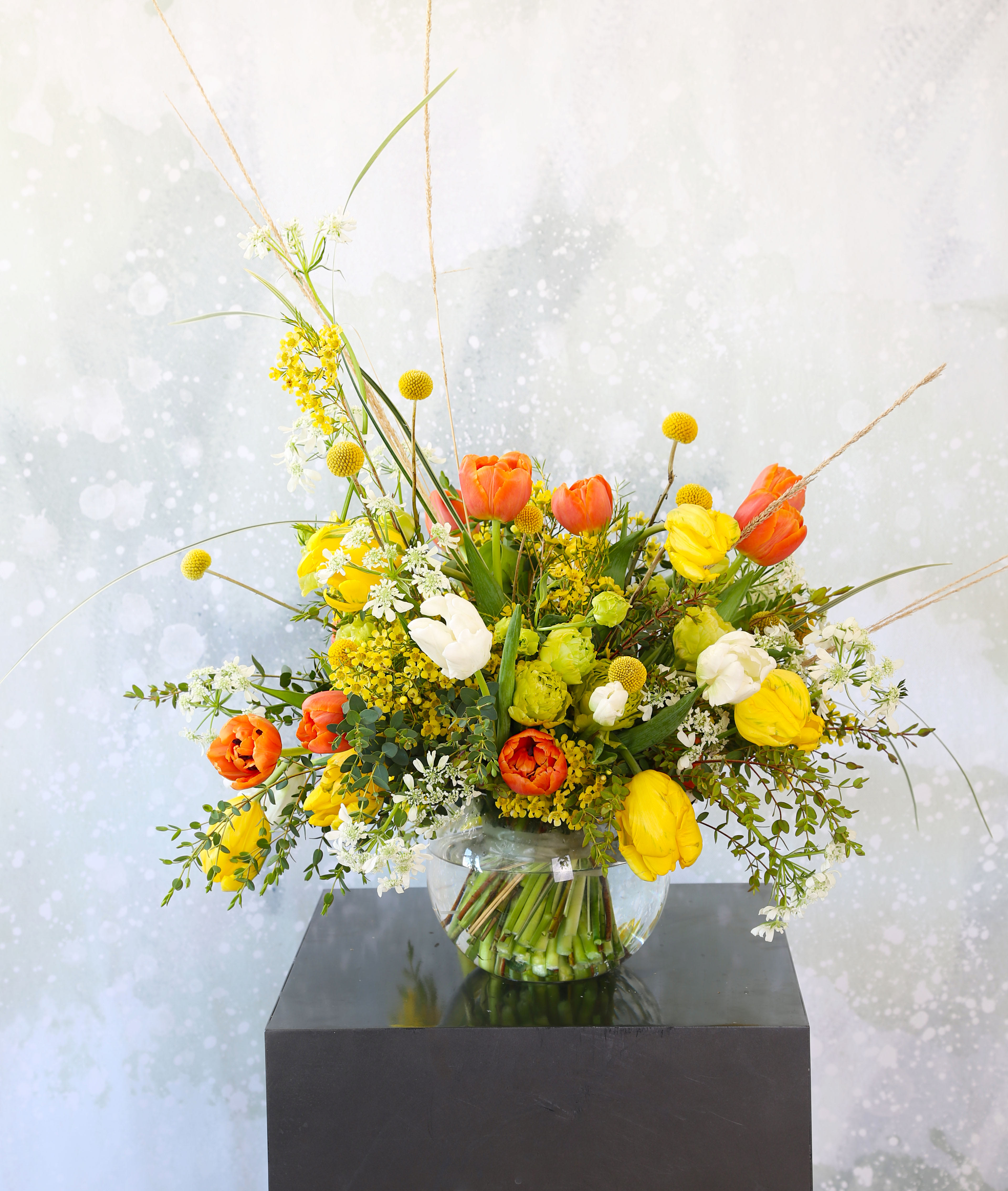 Tulip Spring garden - A cheerful Orange, yellow and Ivory Tulip combination handtie bouquet. This arrangement create with seasonal lisianthus and bloom in 8" ball glass vase