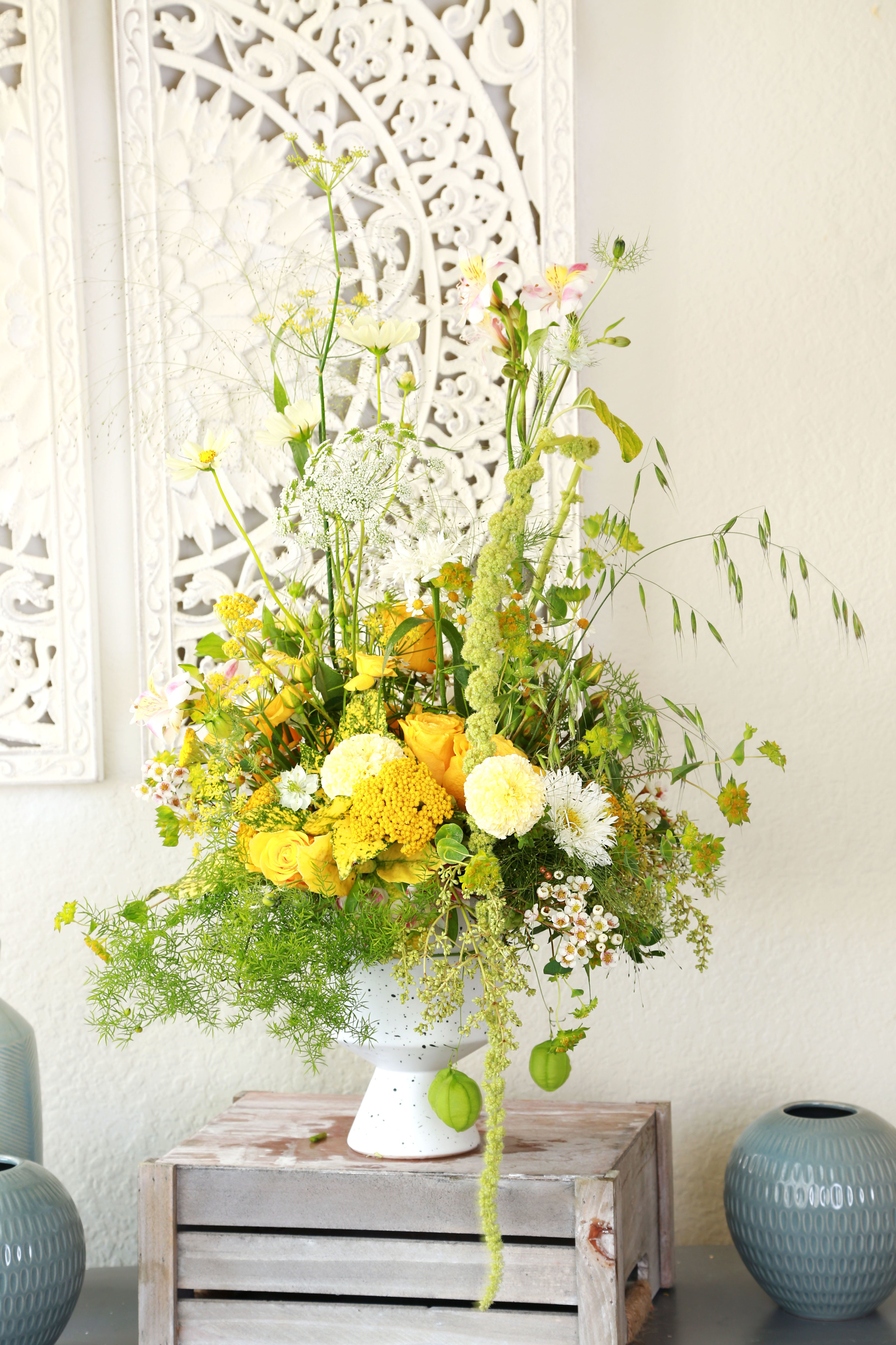 Golden Meadow - Bring sunshine indoors with Golden Meadow, a wild, airy floral arrangement bursting with joyful yellow roses, golden yarrow, creamy carnations, and delicate Queen Anne’s lace. Accented with whimsical grasses, chamomile, and soft greenery, this arrangement evokes the feeling of a breezy summer field. Designed in a speckled ceramic pedestal vase, it’s the perfect centerpiece for brightening up a home, event, or gifting a touch of warmth and natural elegance. Perfect for: Housewarmings, summer gatherings, or simply celebrating nature’s effortless beauty. This arrangement can do in the Ivory 5" opening ceramic vase, but also gold vase per request