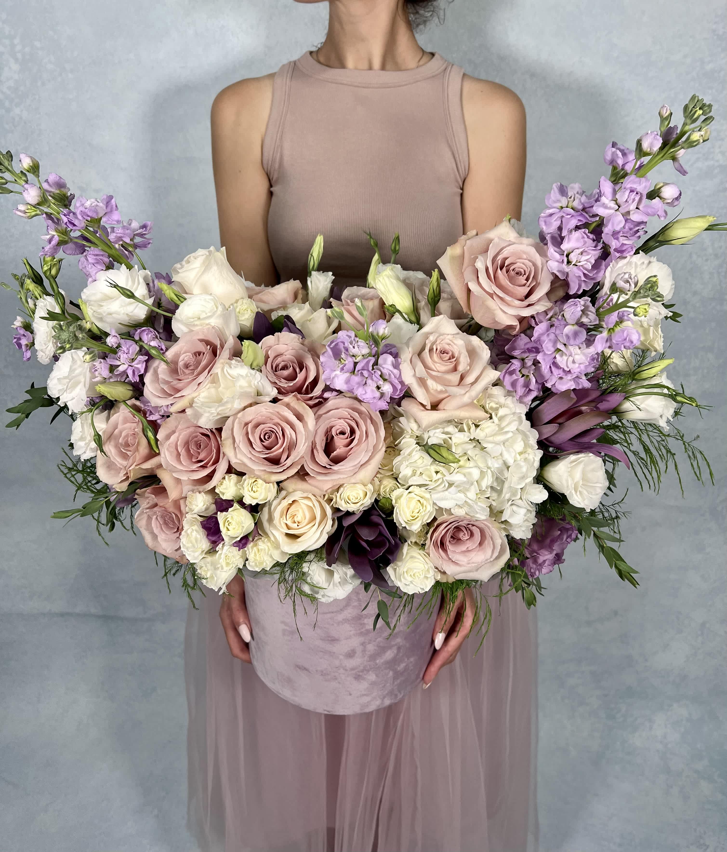 Angel Wings D - This elegant floral arrangement features a soft palette of blush pink roses, delicate lavender blooms, and creamy white hydrangeas. The combination of pastel hues and lush textures creates a sophisticated and romantic display, perfect for weddings, anniversaries, or any special occasion.  DELUXE size is shown in the pictures. 