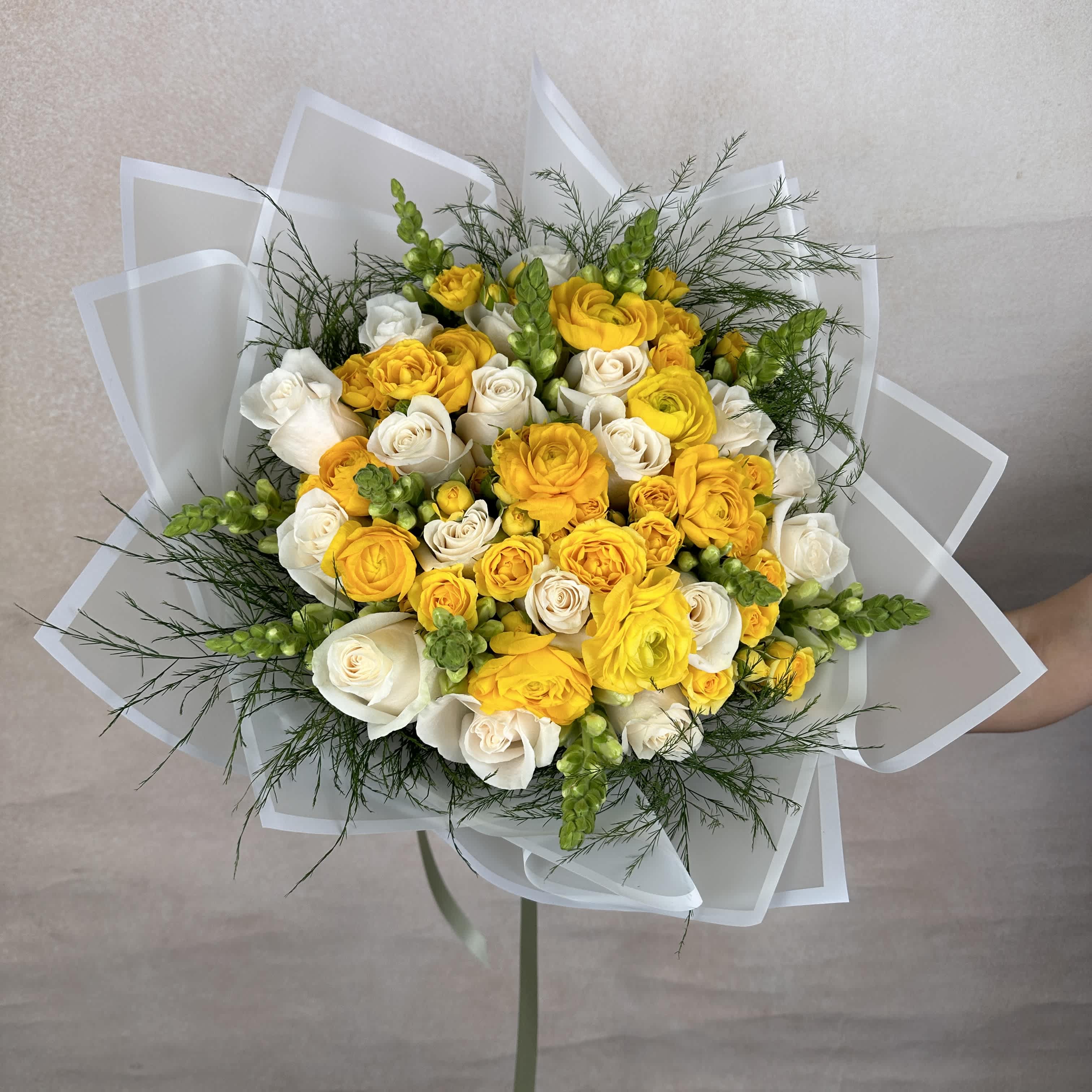 Yellow Delight D - Yellow Delight is a vibrant and elegant bouquet featuring lush roses, striking snapdragons, and cheerful yellow ranunculus, accented with fresh greenery. This lively arrangement blends classic beauty with a touch of whimsy, making it perfect for brightening any space or celebrating a special occasion. DELUXE size is shown in the picture.