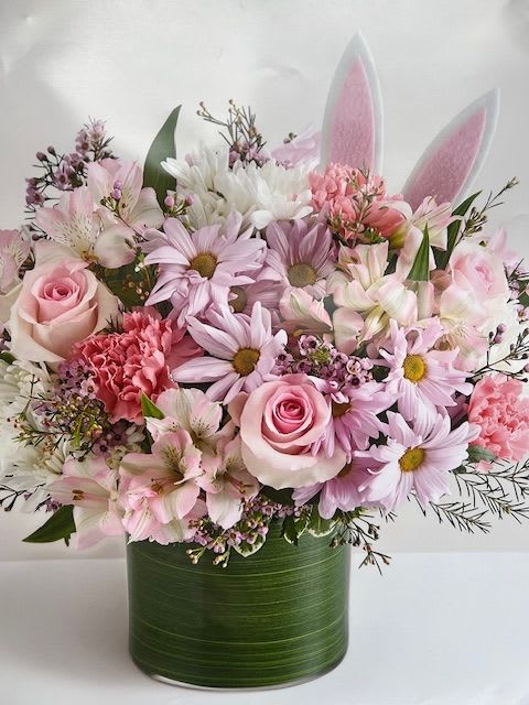 Easter Ears - Soft pastel pinks and lavender mingle with crisp white blooms in a compact, rounded bouquet that feels like a gentle spring hug - perfect as an Easter flower arrangement or a cheerful Mother's Day gift. The playful pair of white-and-pink bunny ears tucked into the center gives    All stems are gathered in a clear glass cylinder vase with a smooth band of green along the inside. The compact, rounded shape keeps the arrangement cozy and easy to display on tabletops or bedside stands.  If you'd like this for a non-seasonal occasion, we can send it without the bunny ears (and without hidden eggs) so it reads more broadly as a birthday, Mother's Day, new baby, or get-well bouquet. Arrives ready to display in the included vase; change the water every few days and trim stems slightly to help blooms last longer.