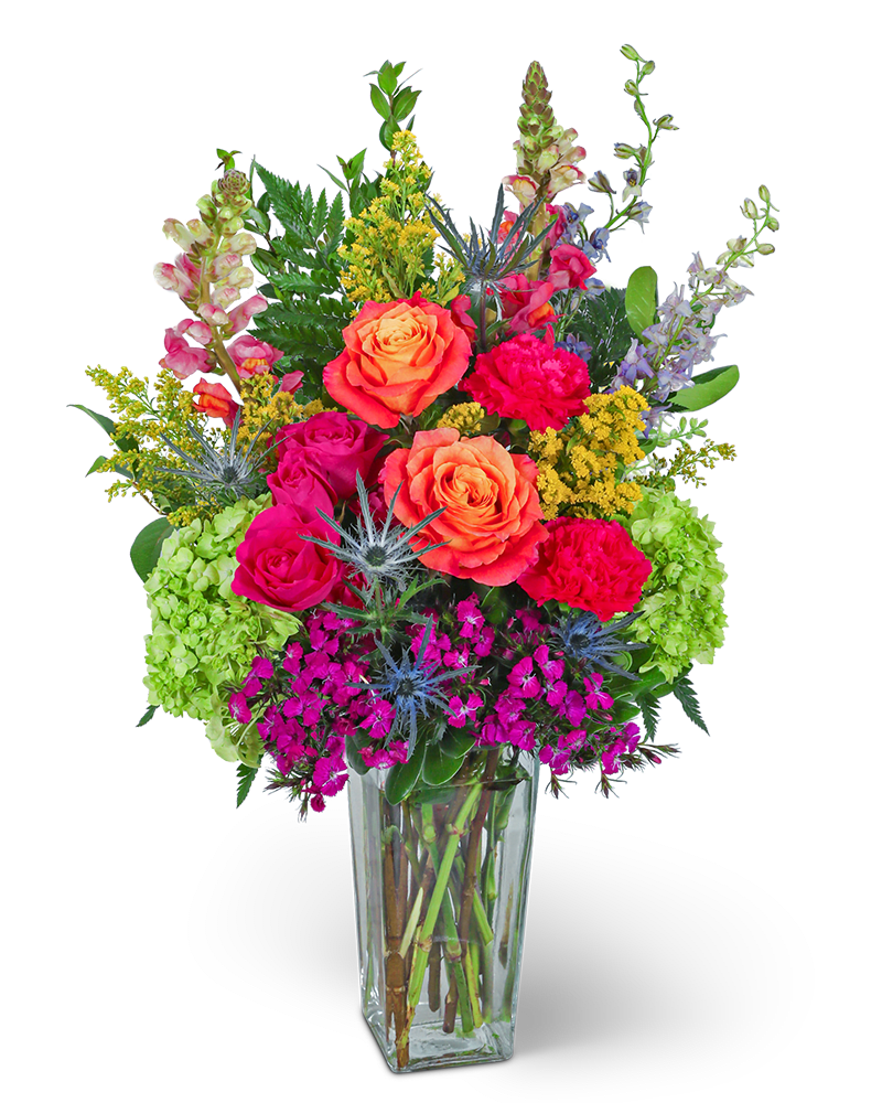Tall arrangement of bright orange roses, hot pink blooms, and green hydrangeas in a clear glass vase.