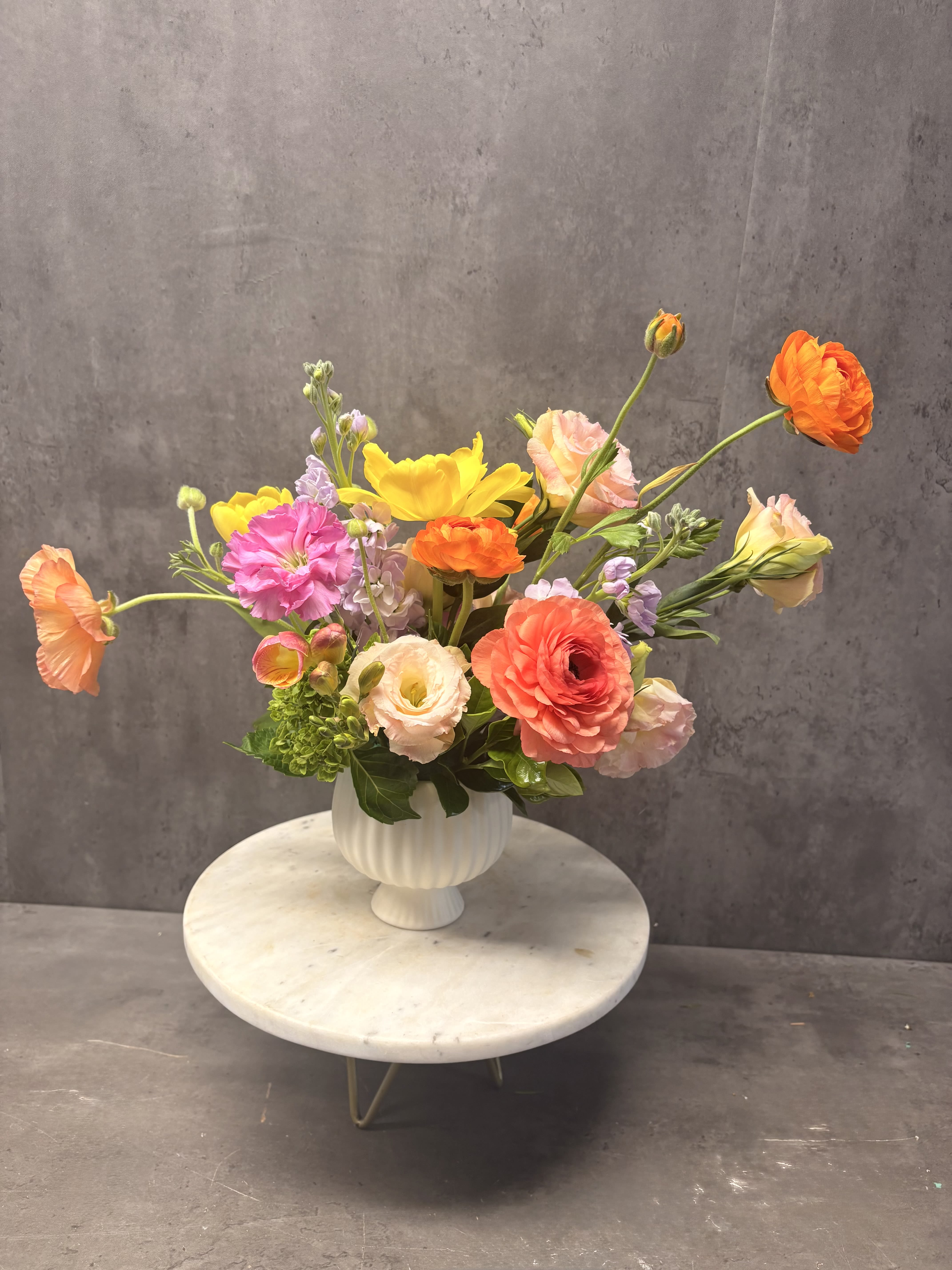 Sprinkle of Spring - Created in a white compote, this petite arrangements brings the cheer of spring. ****flower selection will vary based on seasonal availability***
