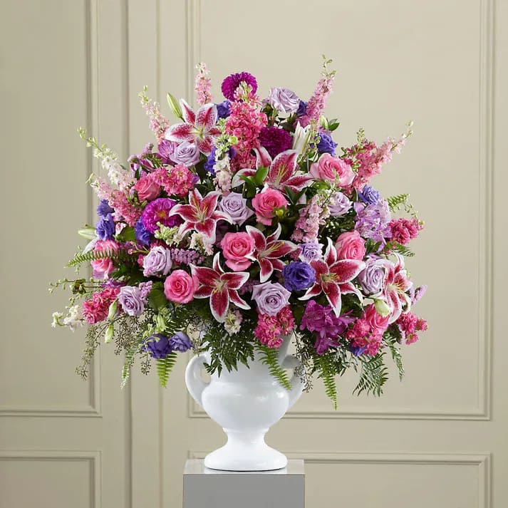 Peaceful Tribute Arrangement - Extravagant, beautiful, and comforting, this generously scaled arrangement eloquently expresses your sympathy with an abundance of love and a profound representation of loss. Handcrafted by our artisan designers, it combines a colorful profusion of lavender and hot pink roses, pink statice, purple lisianthus and dahlias, Stargazer lilies and lavender alstroemeria enhanced with a rich and exotic variety of lush greenery in a classically-inspired white ceramic urn.  Details The Deluxe Arrangement is approximately 38"H x 34"W. Designed by florists, ready to display. Pet Safety Precautions: This bouquet or plant may include flowers and foliage that are known to be toxic to pets. To keep them safe, be sure to keep this arrangement out of your pet's reach.  Bloom Details Rose Stock Lily Larkspur Dahlia Alstroemeria