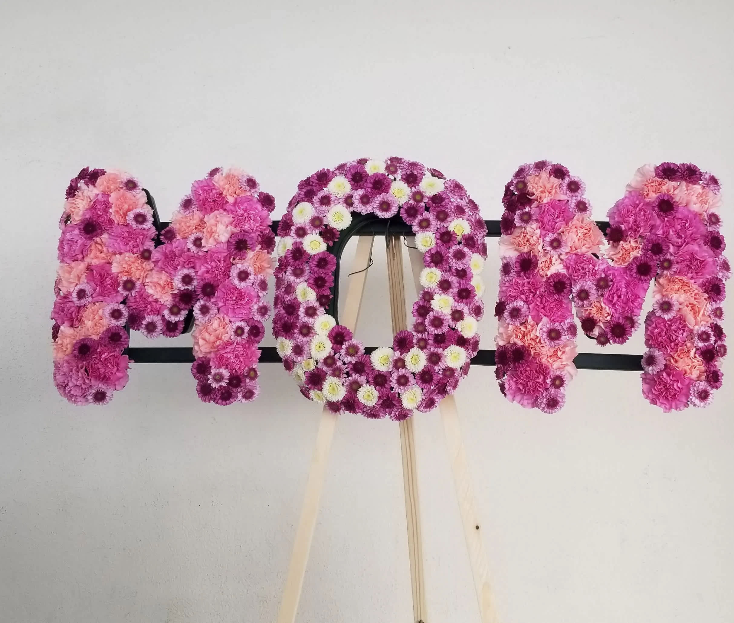 MOM Tribute spray - The Remembering Mom Arrangement honors the life and the love you have for your mother at her final farewell service. Light pink spray roses, white cushion poms,  are artfully arranged to spell the word, MOM creating a wonderful memorial for the woman who continues to shape your life's journey. Flowers can be ANY colors. Approx 36 inches wide by 10 inches high You may request different colors, please note in the Special Instructions.