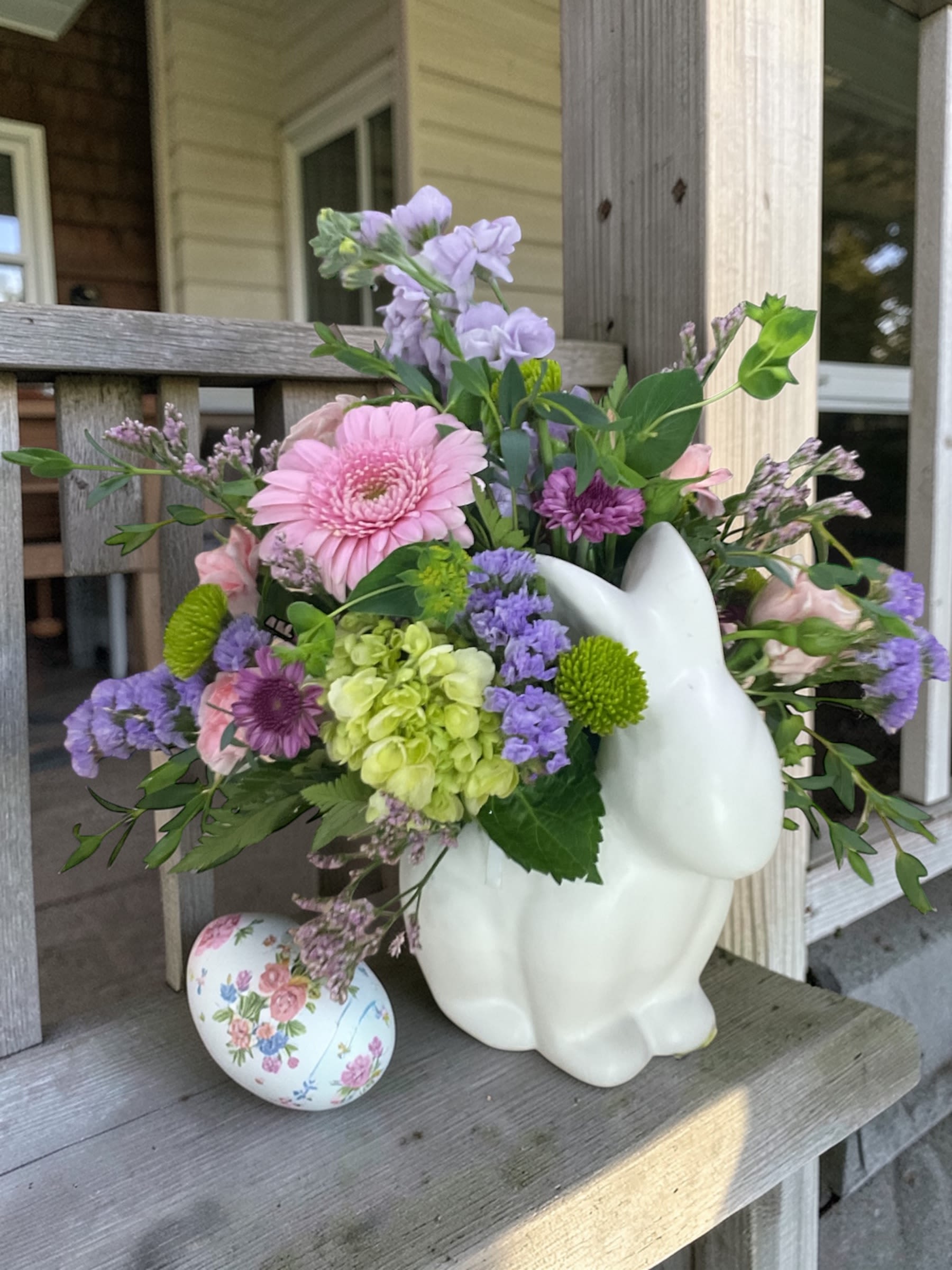 Good Hare Day - Good Hare Day   A fresh take on Easter, Good Hare Day is a cheerful spring arrangement designed in an adorable ceramic bunny keepsake container. Featuring a soft blend of pinks, lavenders, and fresh greens—highlighted by a vibrant gerbera daisy, hydrangea, and seasonal blooms—this piece brings just the right amount of color and charm to any space.  Light, airy, and full of personality, it’s perfect for Easter gifts, spring birthdays, or anyone who could use a little pick-me-up after a long winter.  The best part? When the flowers are gone, the bunny stays—making it a sweet keepsake long after Easter has passed.  A compact design approximately 10” tall and 10” wide. 