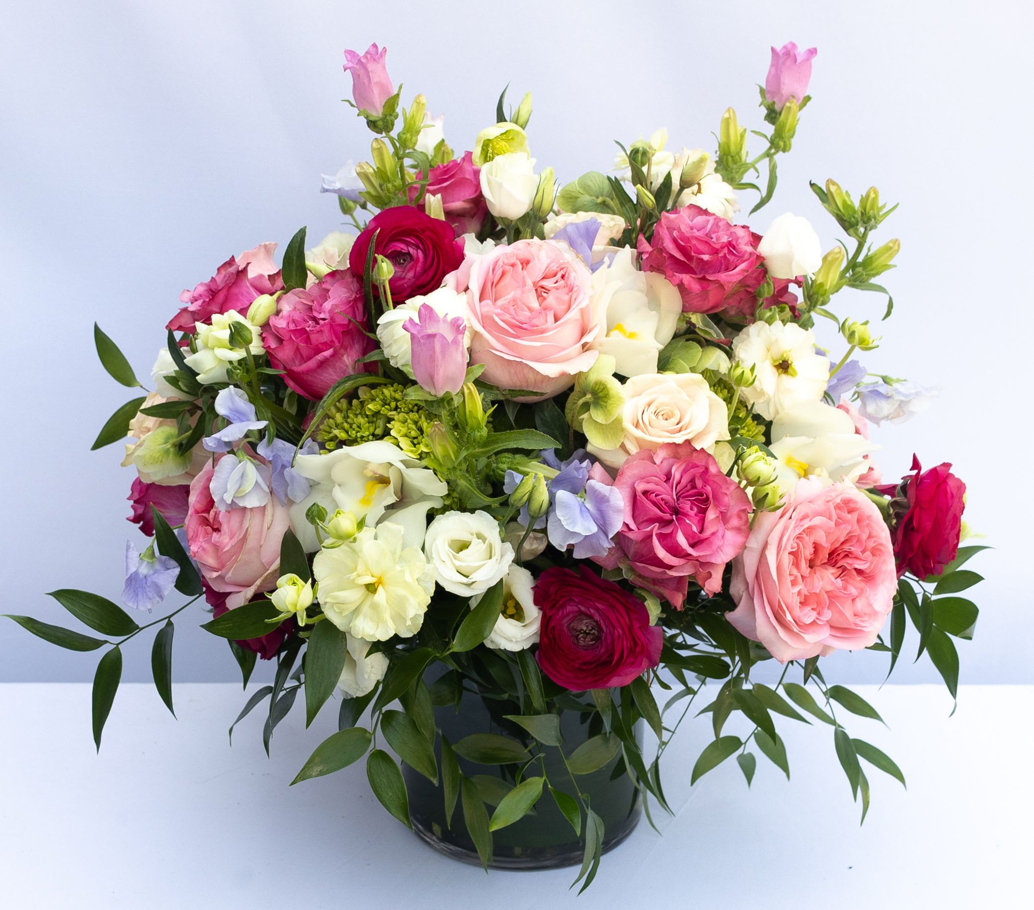 Garden Luxe - Lush arrangement in a 6x6" glass cylinder. Flowers may include a variety of garden roses, ranunculus, cymbidium orchids, campanula, and sweat peas.