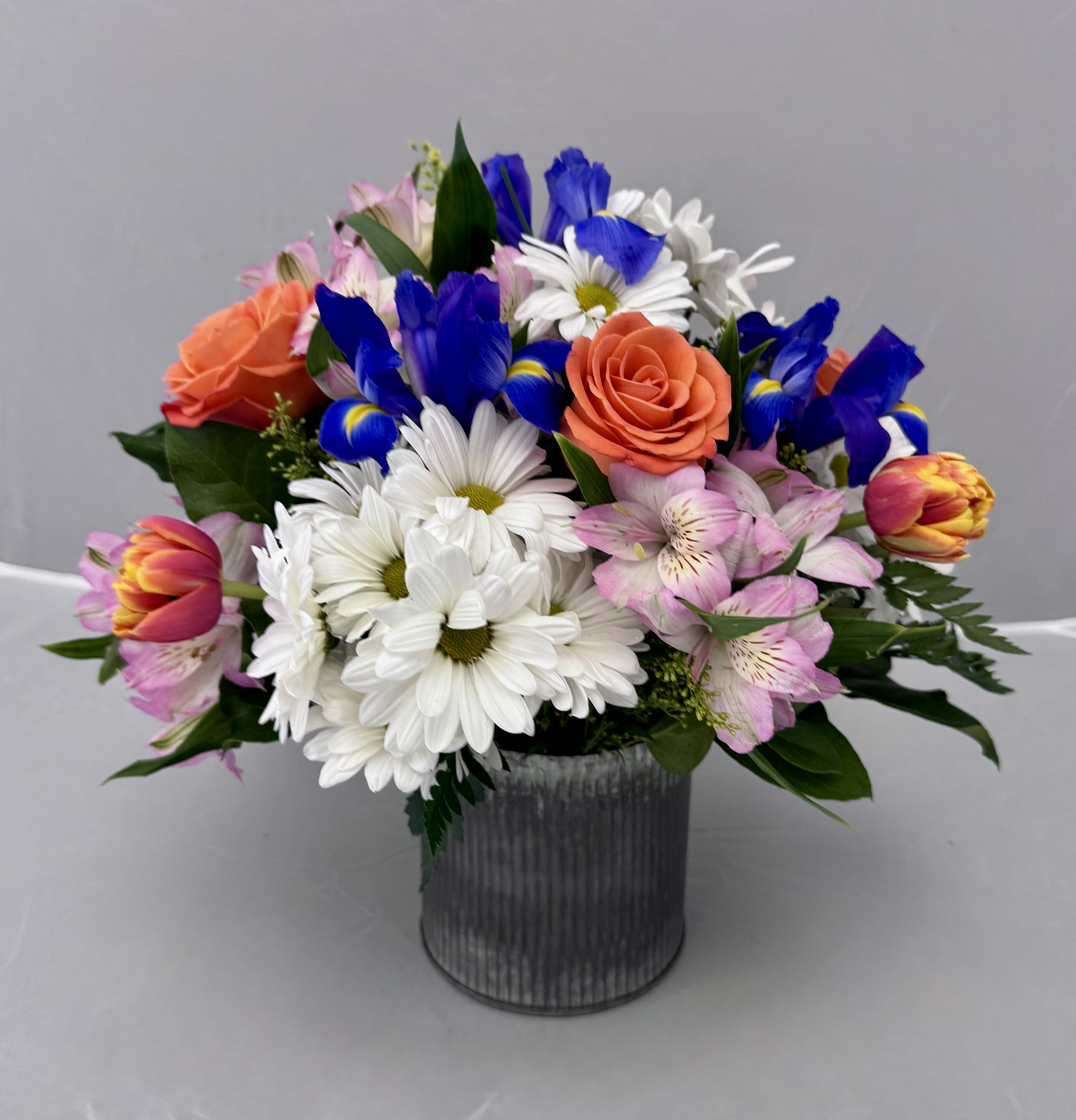 Mixed bouquet of daisies, roses, tulips, and alstroemeria in a metal vase