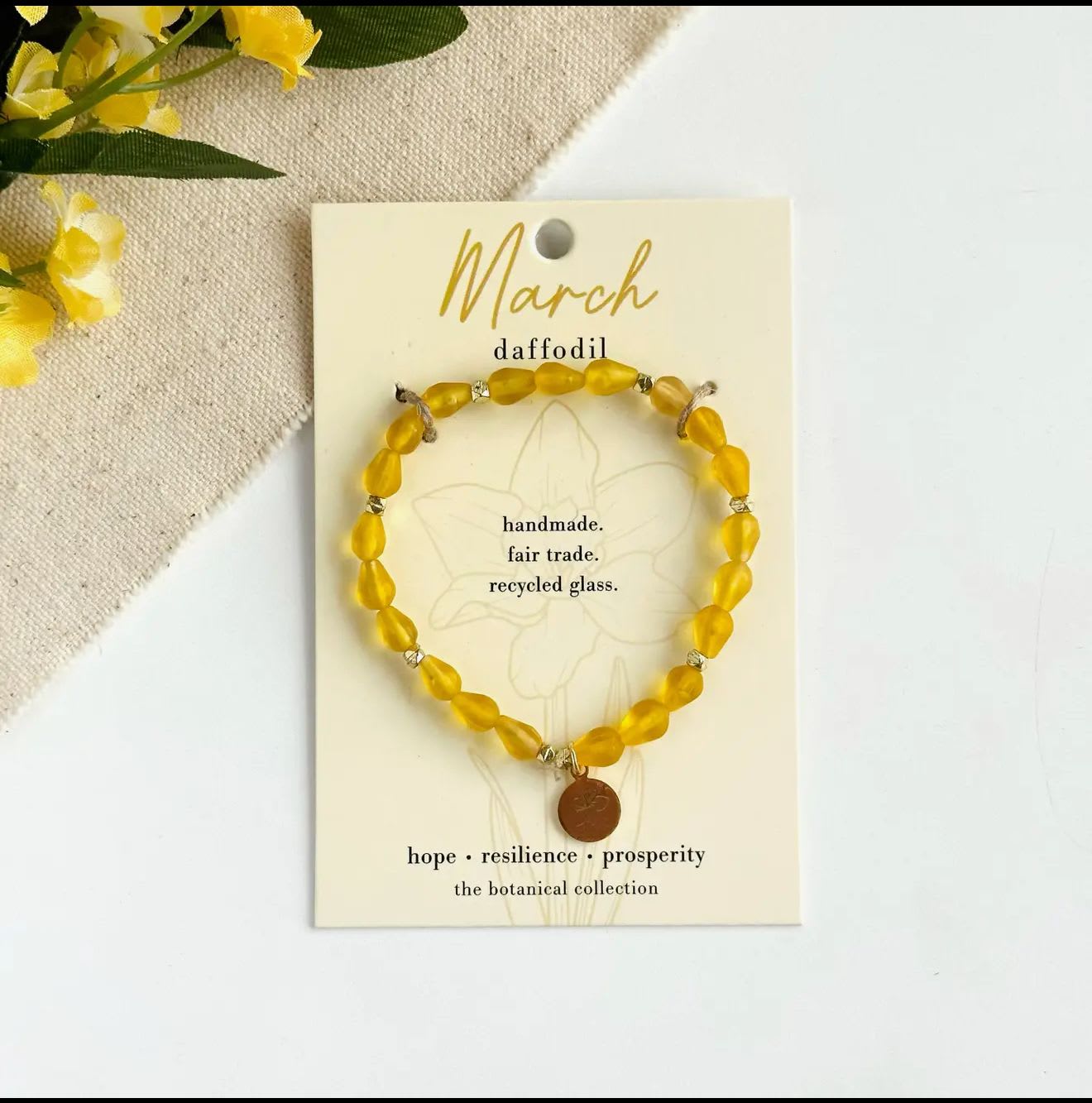 March-Birth Flower Bracelet - Hello, March!  Part of our Botanical Collection, the March Bracelet is crafted from bright yellow glass beads, brass accent beads, and features a daffodil charm. Great for gifting, the card features the daffodil and it's symbols of hope, resilience and prosperity, along with a garden-inspired quote. This bracelet also benefits an urban community garden project!  The semi-opaque beads have a satin, frosted texture and are handmade from recycled glass. The flower charm is 24k gold plated.   Sustainably handmade by women artisans in India.