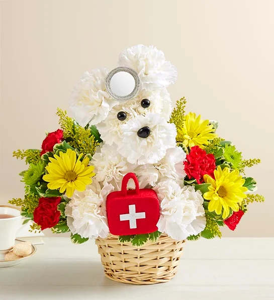 Doggie Howser M.D. #146761 - Our doggie doctor provides a sure cure for anyone feeling down or under the weather. And best of all, he's always willing to make house calls! This medical mutt, part of our signature a-DOG-able litter, has been hand-crafted by our expert floral "surgeons" from fresh white carnations, vibrant poms, solidago and waxflower. Ready to brighten anyone's day, it's the perfect prescription for creating smiles. Hand-designed a-DOG-ableÂ® arrangement of white carnations, poms, solidago, waxflower and variegated pittosporum Crafted by our florists in the shape of an adorable dog, complete with eyes and nose Doggie doctor arrives carrying a plush doctor bag, complete with headpiece and stethoscope Designed in a playful willow dog bed basket lined with moss Arrangement measures approximately 11"H x 11"L Our florists select the freshest flowers available so floral colors and varieties may vary