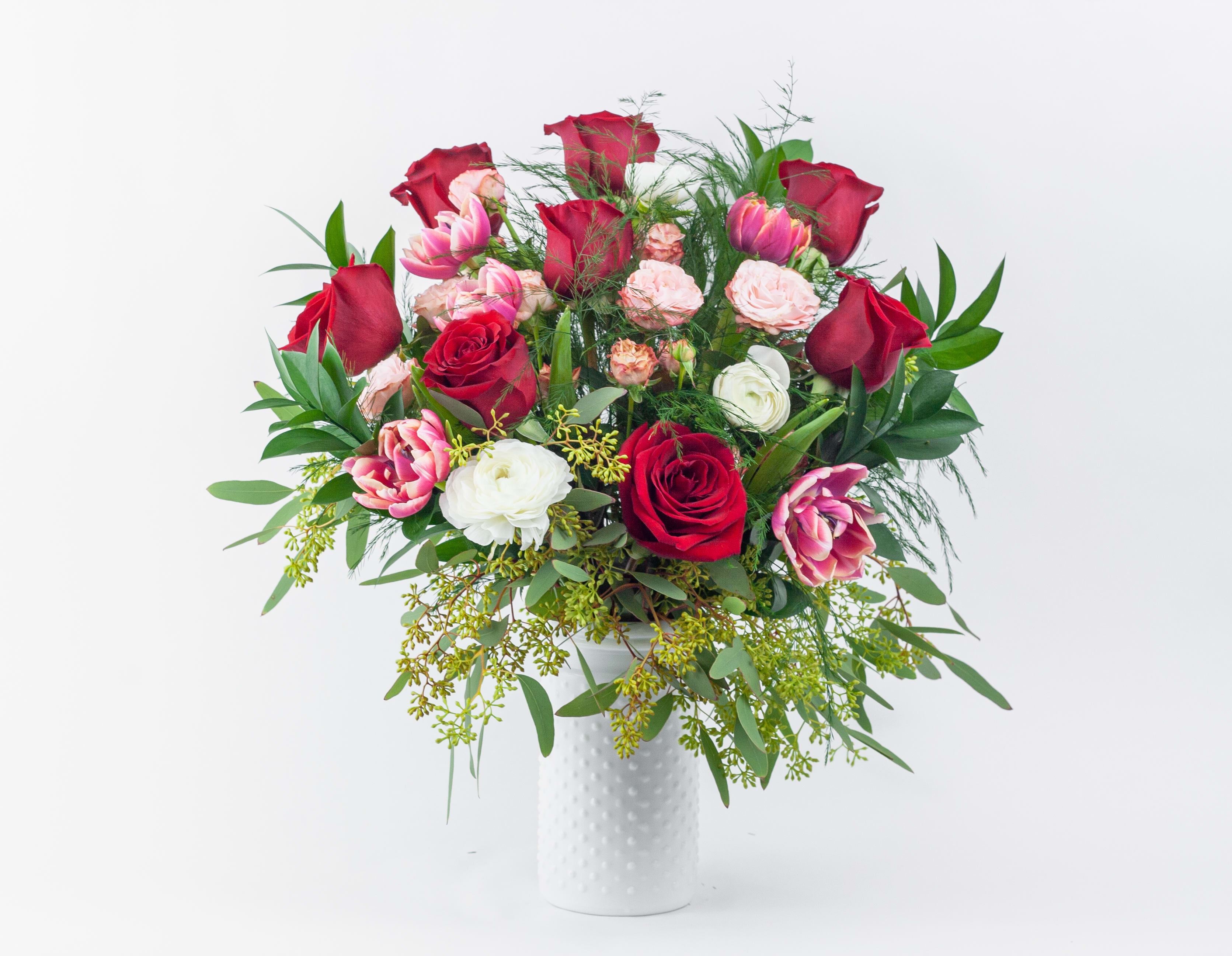 Bouquet of red and pink roses with white blooms in a white vase